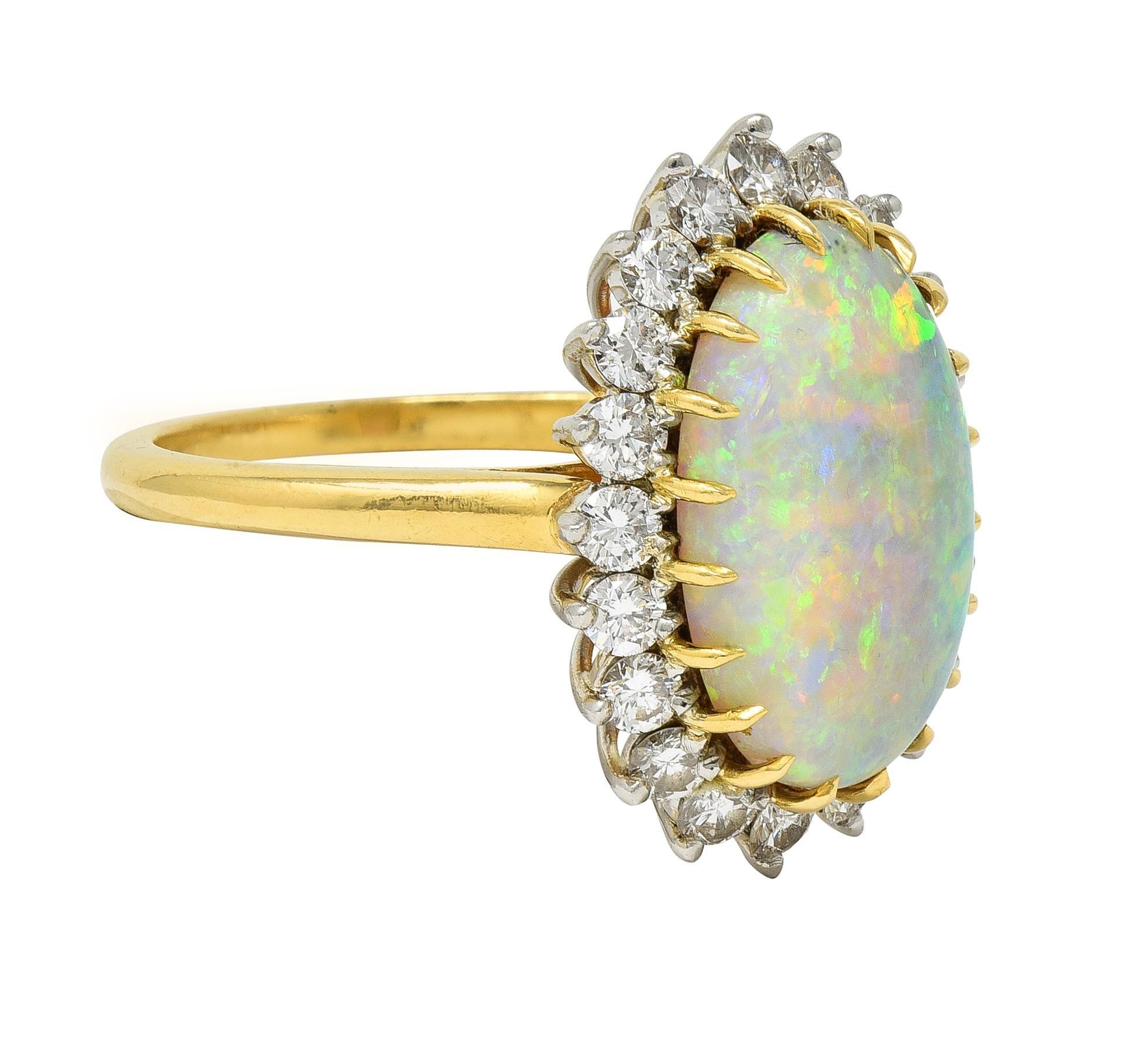 Centering an oval-shaped opal measuring 9.5 x 5.3 mm - translucent white in body color with spectral play-of-color
Set with yellow gold talon prongs with a recessed platinum halo surround of round brilliant cut diamonds 
Weighing approximately 0.80