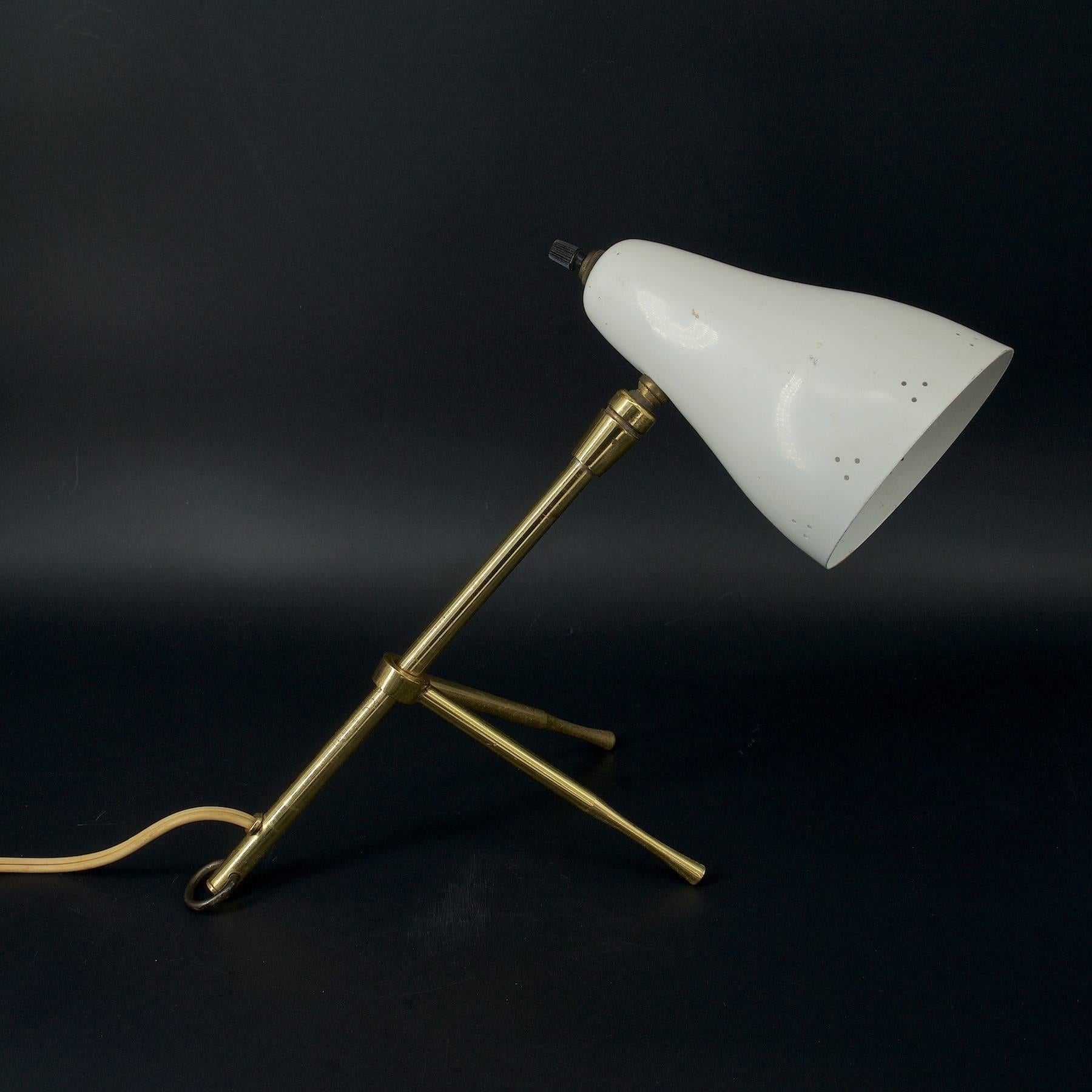 Ochetta adjustable sliding tripod table lamp, can be hung on wall. Patinated brass, off-white enameled pierced conical aluminum articulated hood/shade. Etched serial numbers.
 