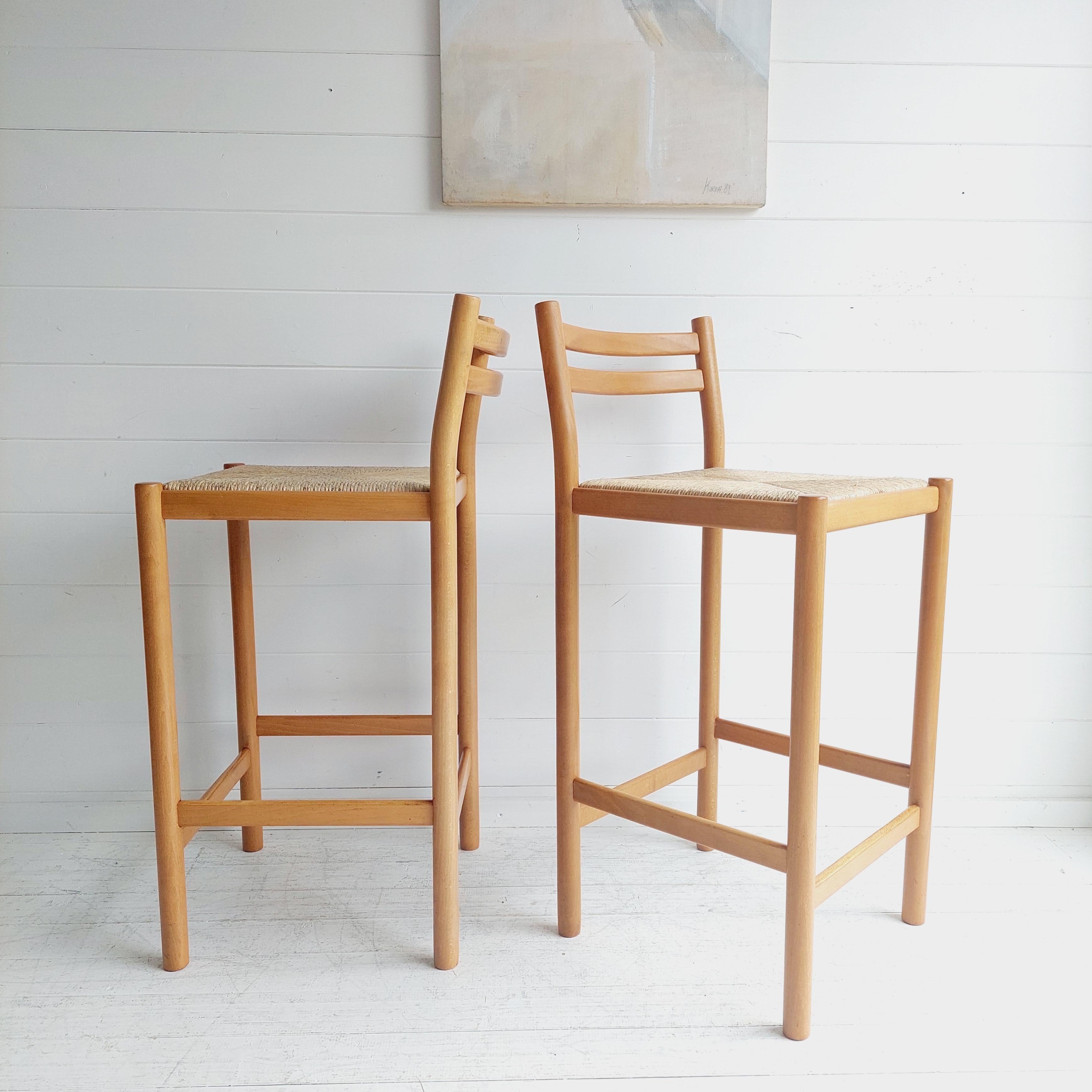 Midcentury bar stool pair.
circa 1970s, England.
Designed in the style of Vico Magisretti for Cassina, circa 1960s, Italy.

Rush seats, beech frame
Rounded wood frame has a curved, laddrered back and a wide, hand rushed seat that begs you to