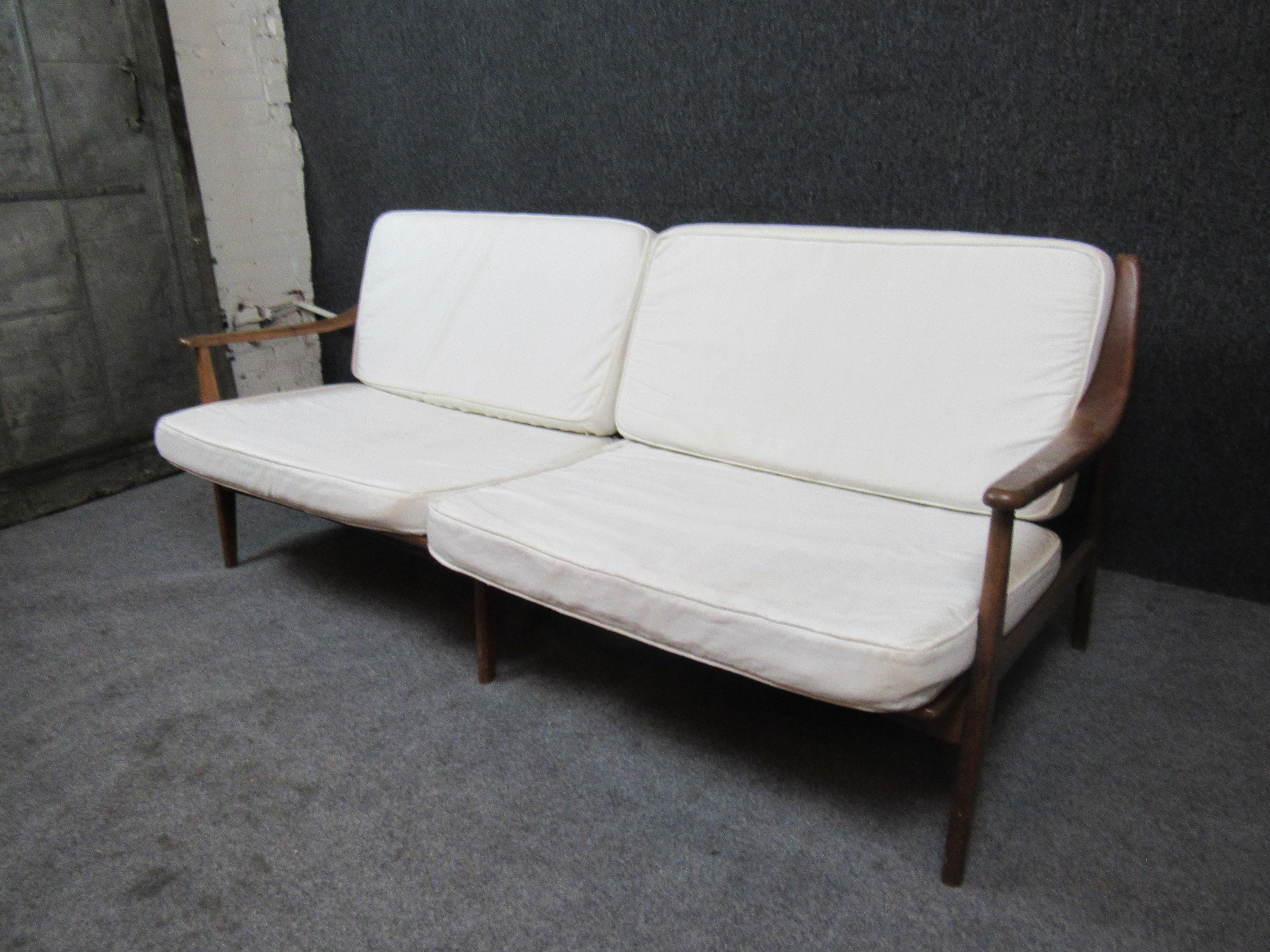 Bring home authentic Scandinavian midcentury design with this charming carved sofa. Borrowing influence from the timeless designs of artists such as Peter Hvidt and Finn Juhl, this minimalist settee features gently sloping arm rests, an attractive