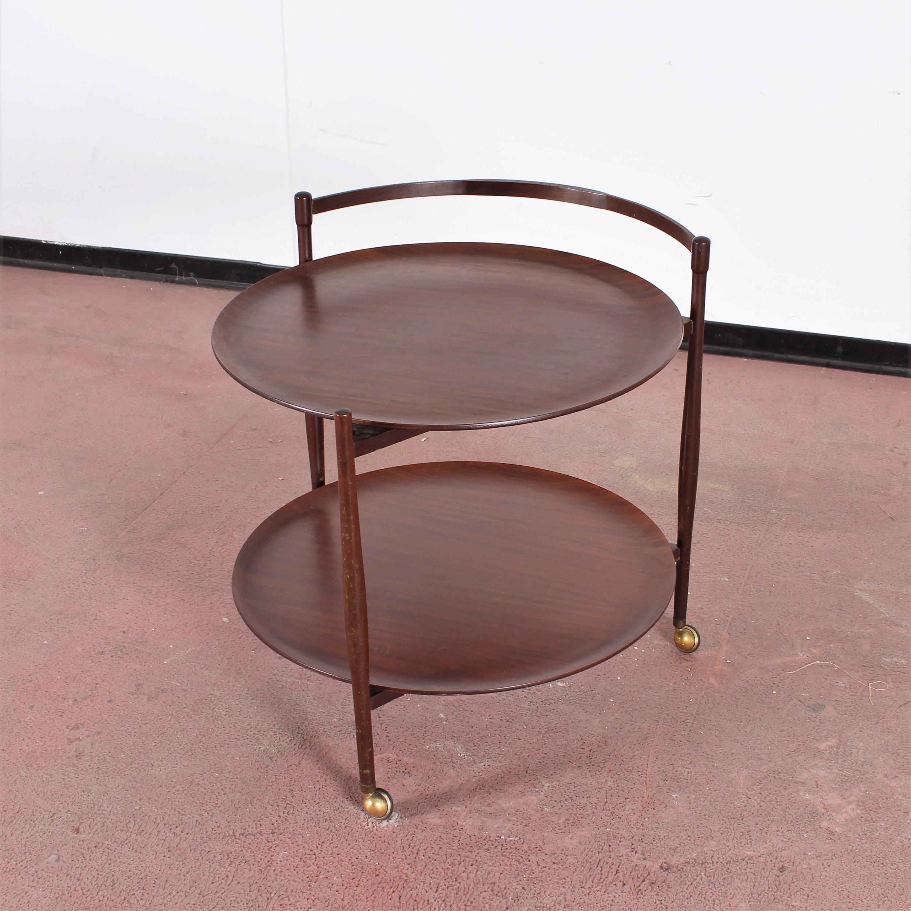 Vintage teak bar trolley with three brass wheels and two large removable circular trays, on two levels.
Signs of use on the back of a tray, highlighted in the photo, Italy, 1960s.
Wear consistent with age and use.