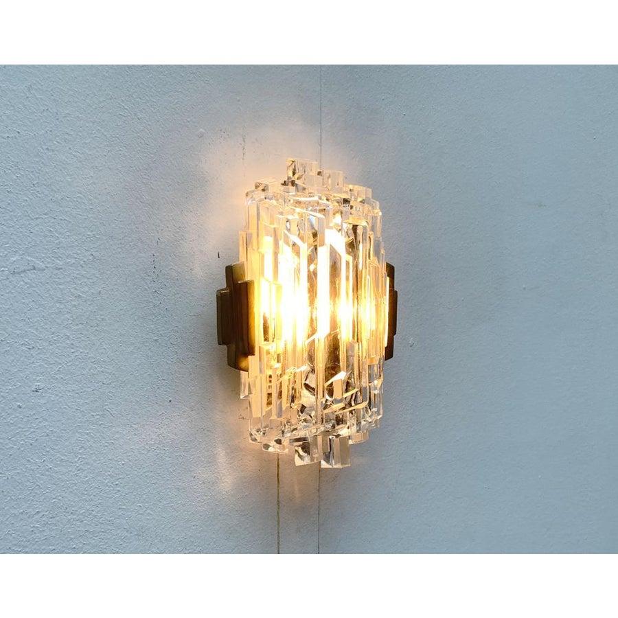 Imponente aplique de pared de Orrefors.

El detalle central de la lámpara es el gran elemento de cristal helado, que cubre casi todo el frontal. El vidrio está formado por varillas en forma de prisma, que en su suma y superposición forman una