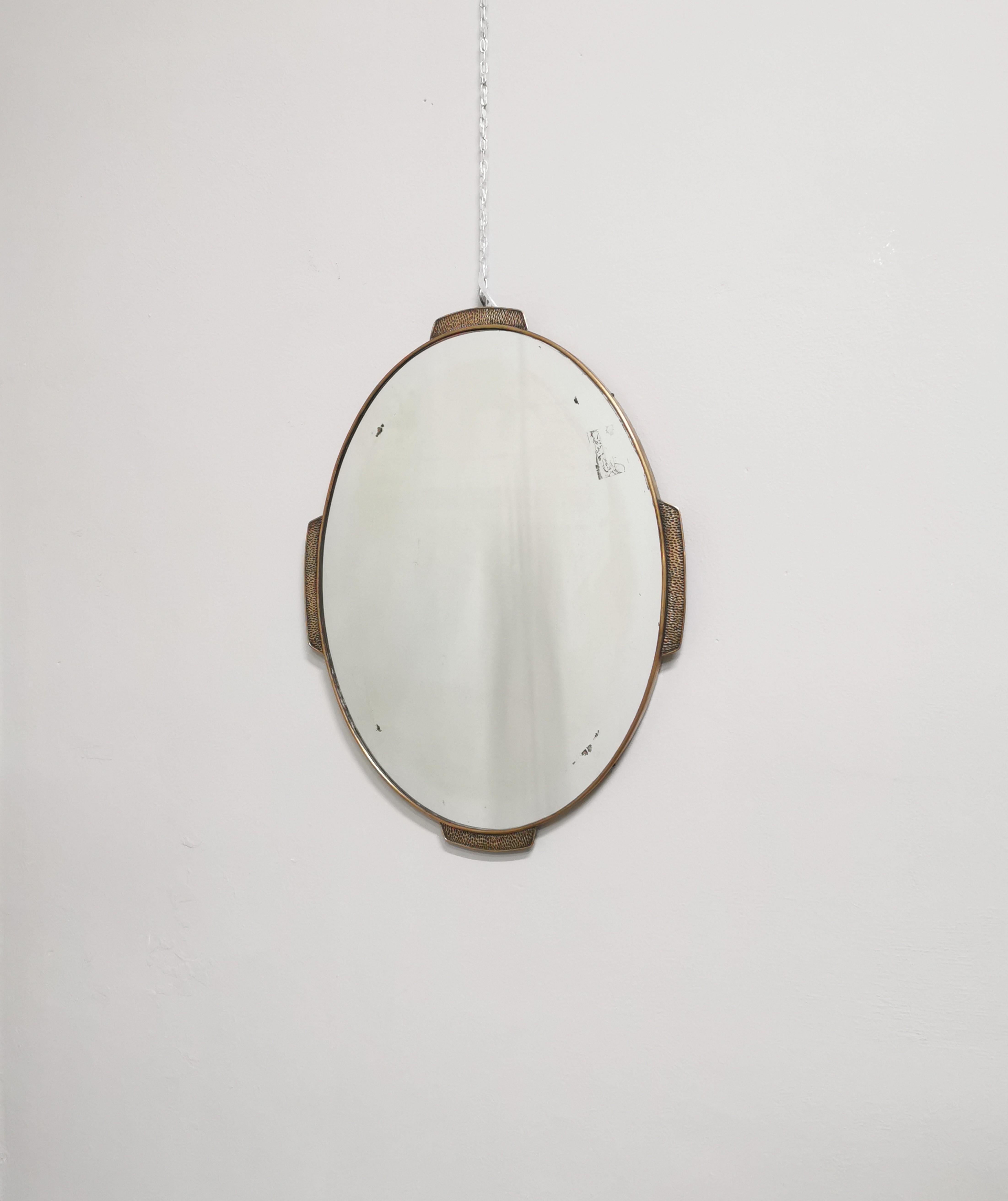 Rare and particular wall mirror by an unknown designer, oval-shaped with brass border and 4 hammered brass decorations. The mirror has a wooden frame. Italian production of the 1950s.