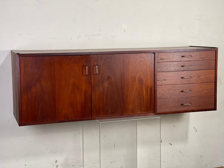 Excellent custom wall mounted media cabinet by Jens Risom; 1950's. In clean original condition - the oiled walnut book matched grain doors and drawer fronts carriy years of patina that make this walnut look like nicely aged. Moveable shelves -