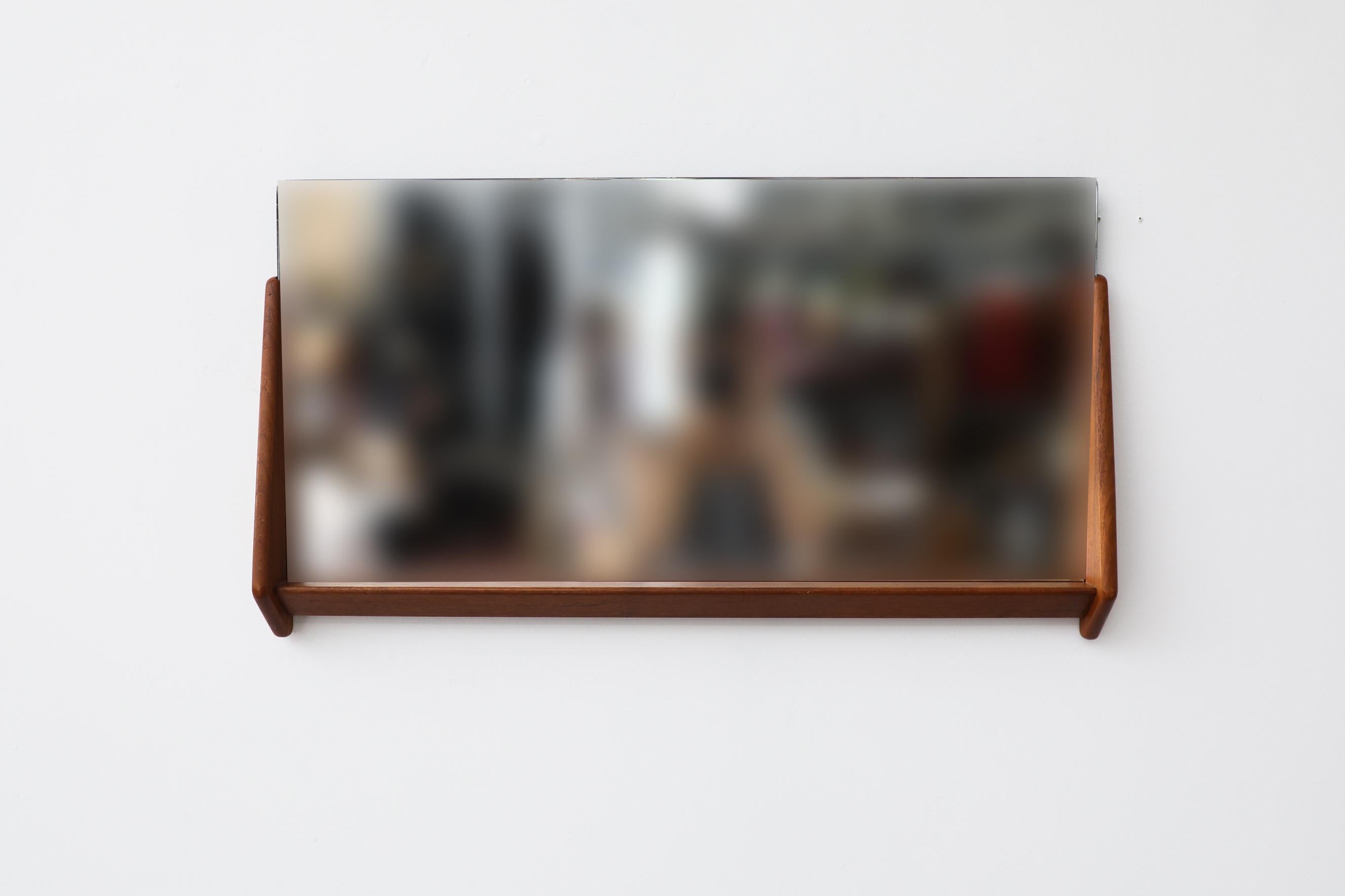 Horizontal wall mounted mirror with teak frame on the bottom half of the mirror, extending slightly on each side and creating a mini shelf under the mirror. The frame has been lightly refinished. The mirror slides into the frame and is in original