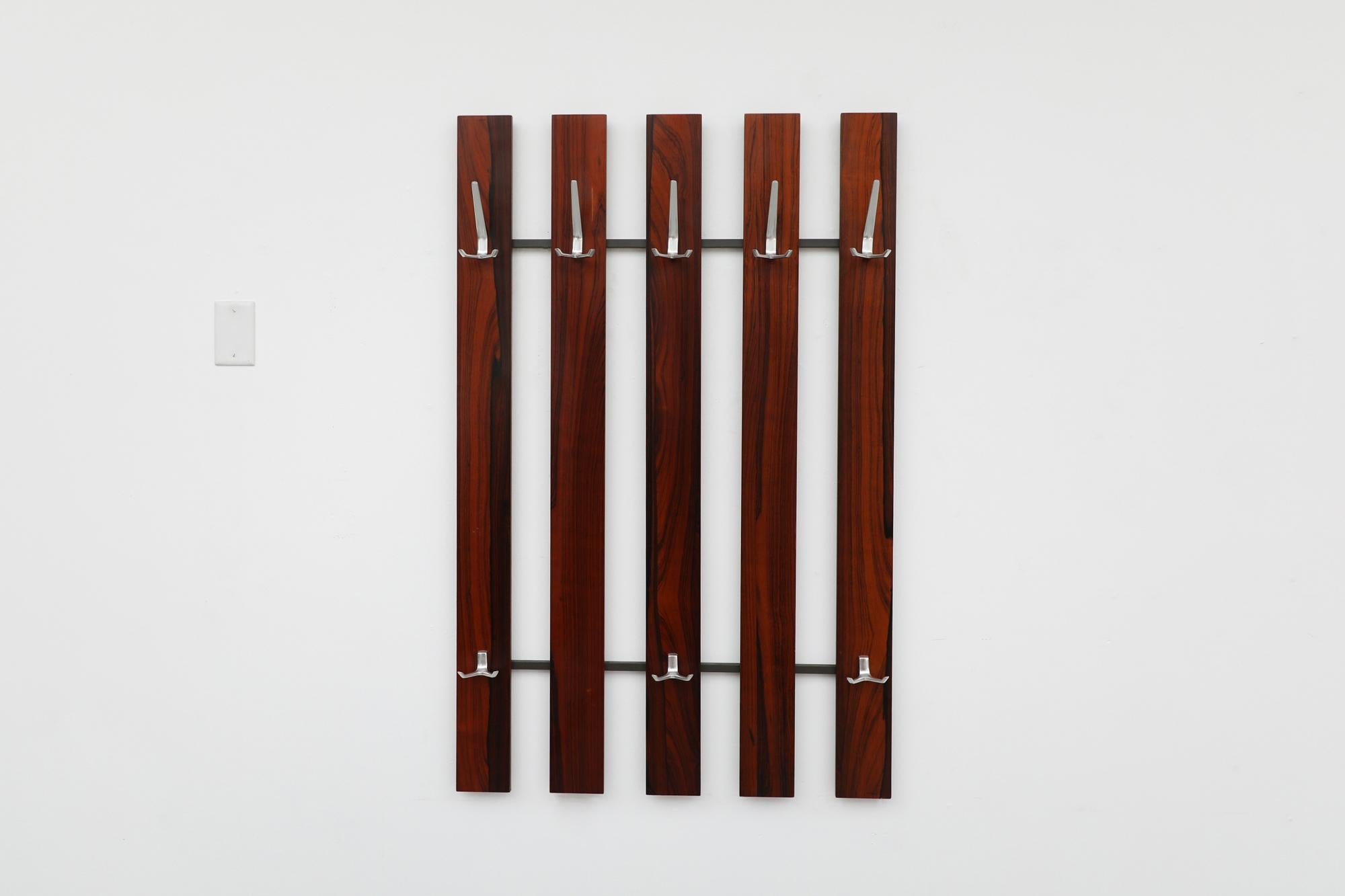 Mid-Century Rosewood wall mounted coat rack with long striped woodgrain pattern. 5 section slats and 8 cast aluminum hooks. In original condition with minimal wear and scratching. Similar coat racks also available and listed separately.