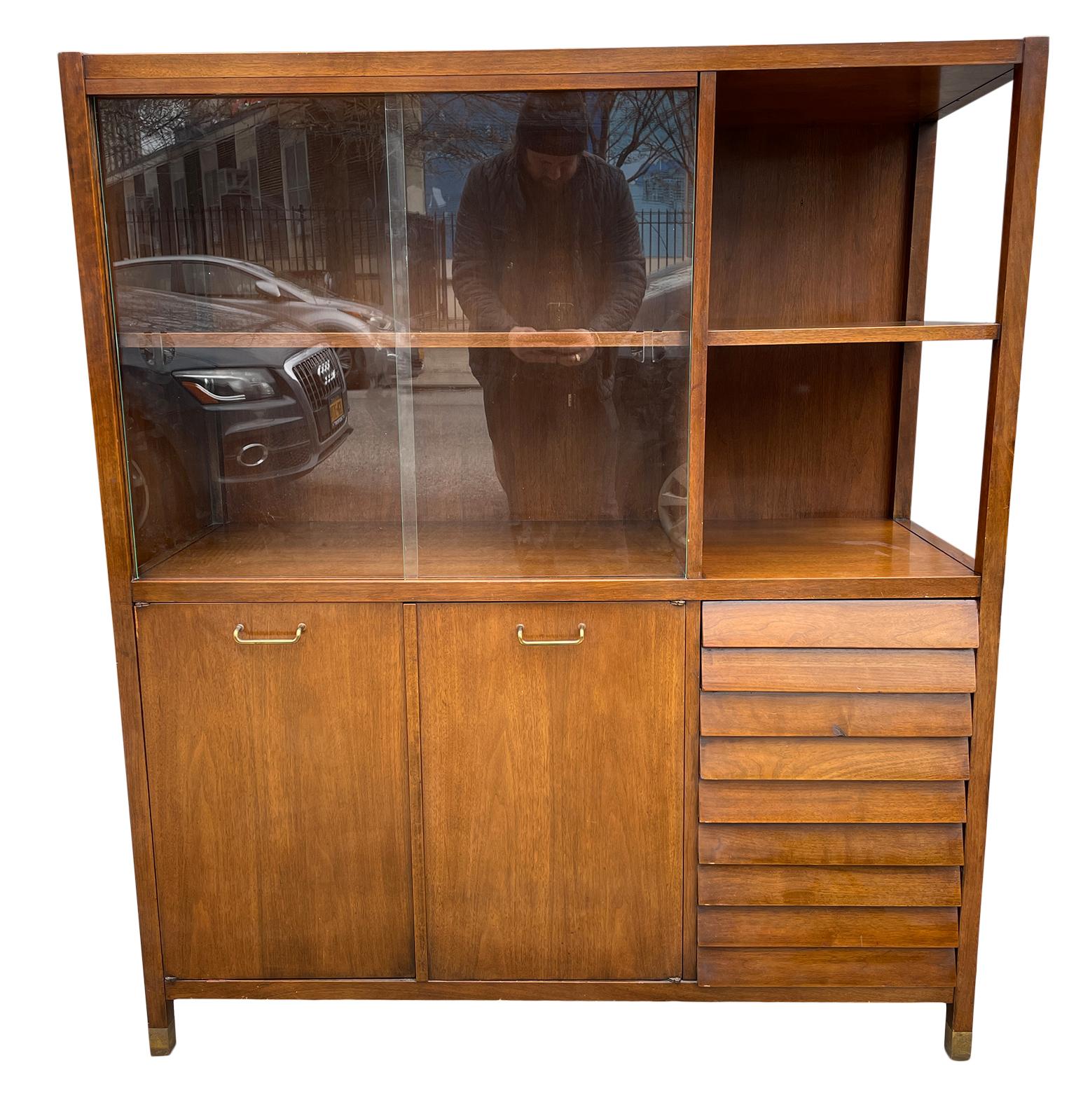 Wall unit cabinet for the Dania Series by Merton Gershun for American of Martinsville. 2 glass sliding doors with lower cabinet and 4 Lou reed drawers on the lower right. Brass handles and feet. Dark walnut finish. Labeled inside drawer. Located in