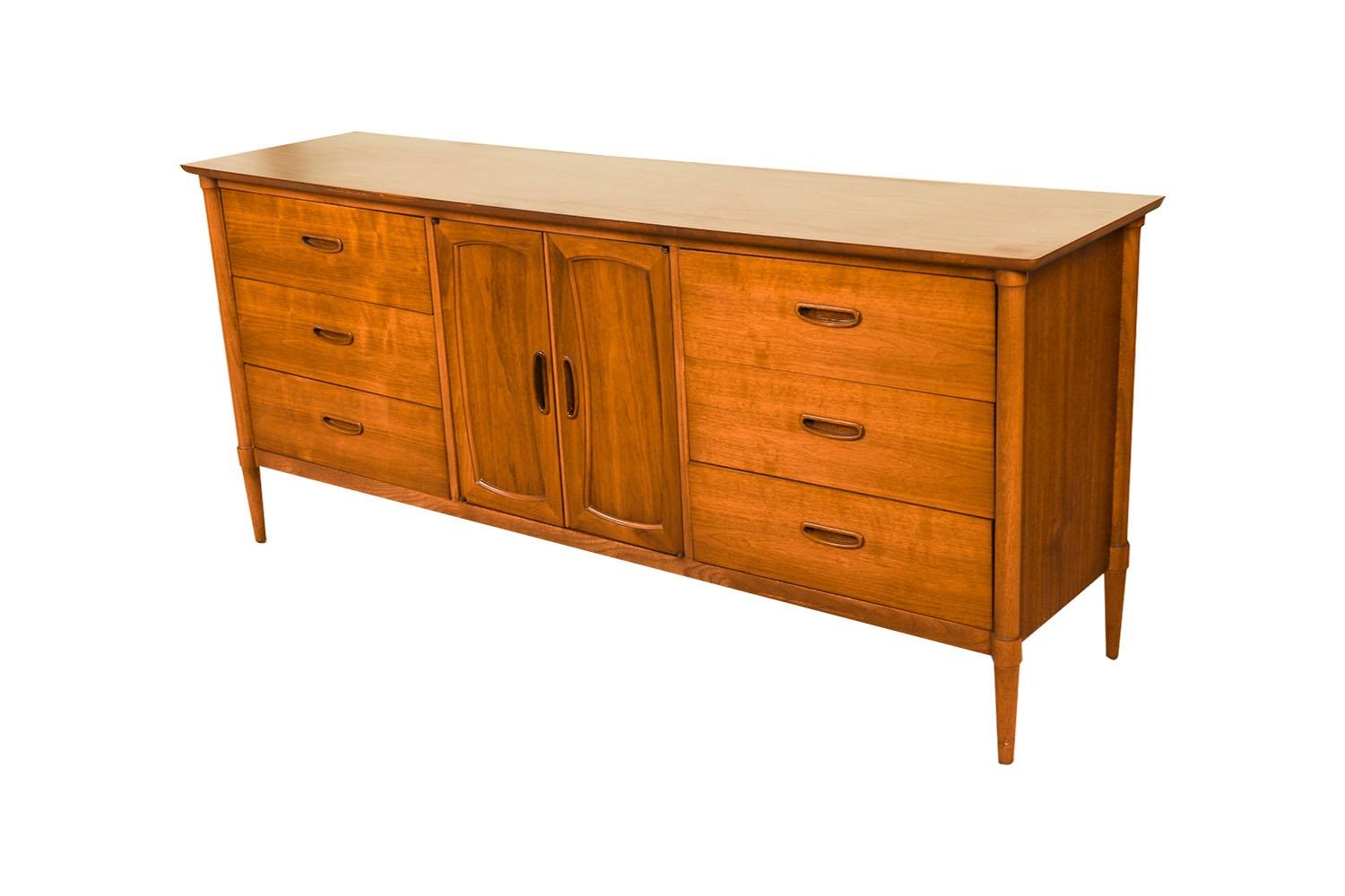 A classic Mid Century Modern walnut dresser or sideboard by Lane Furniture Company. This vintage walnut dresser features a beautiful laminate top, six dovetailed drawers, adorned with beautiful sculpture pulls, flanking two centered doors that open