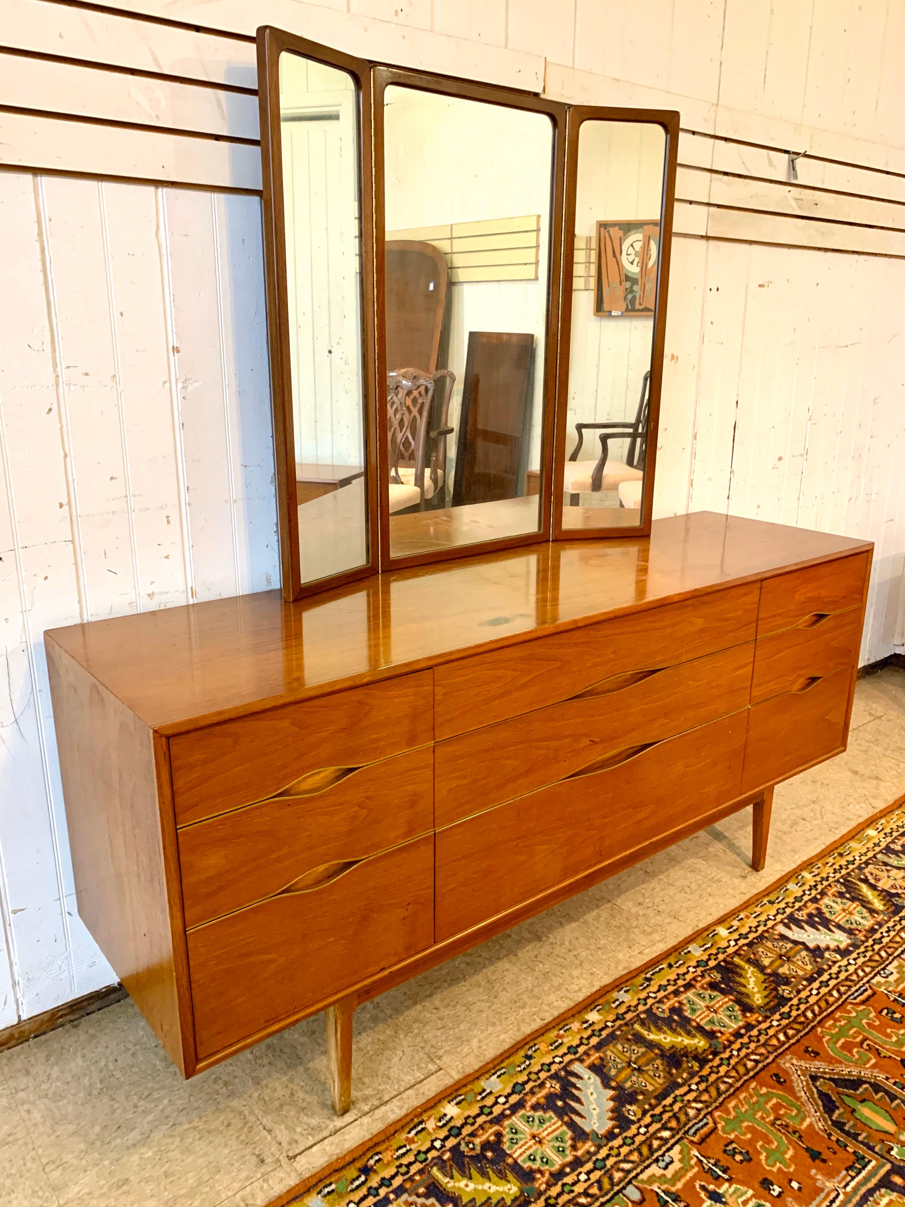 Mid-Century Modern walnut dresser with brass at drawers. Mirror measures 36” W x 39” H.