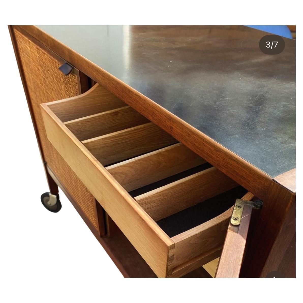 Mid century walnut and cane bar cart on casters by Jack Cartwright Founders. All walnut bar cart with cane front cabinet doors and black laminate top. The inside on left is (1) adjustable shelf and on the right (2) drawers with dividers. Cabinet