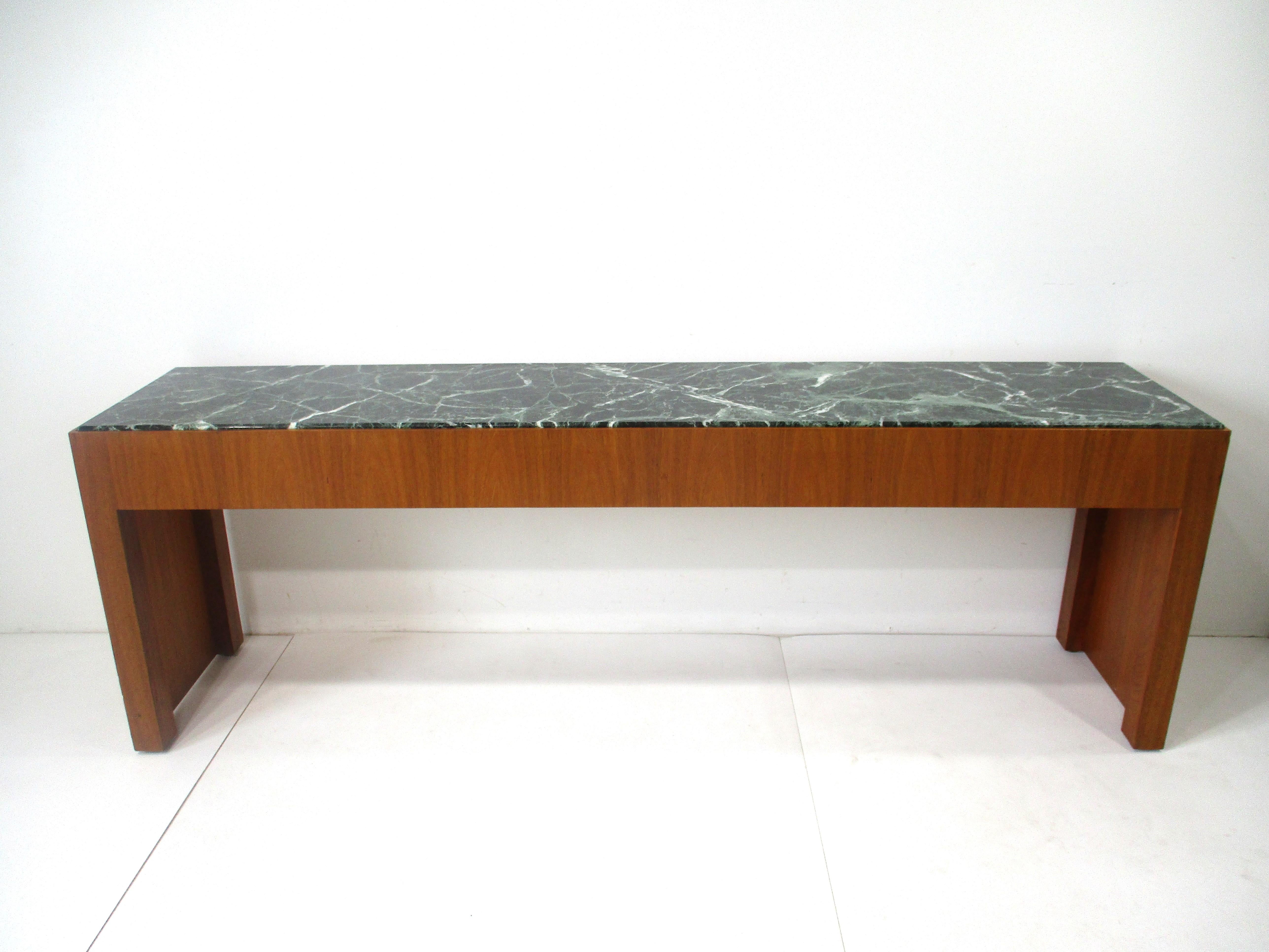 A very well crafted walnut based console table with a dark green and veined beveled edged inset marble top . The one side has a pull out drawer for smalls if used in an entrance way like keys and mail . This piece can be used in any interior or room