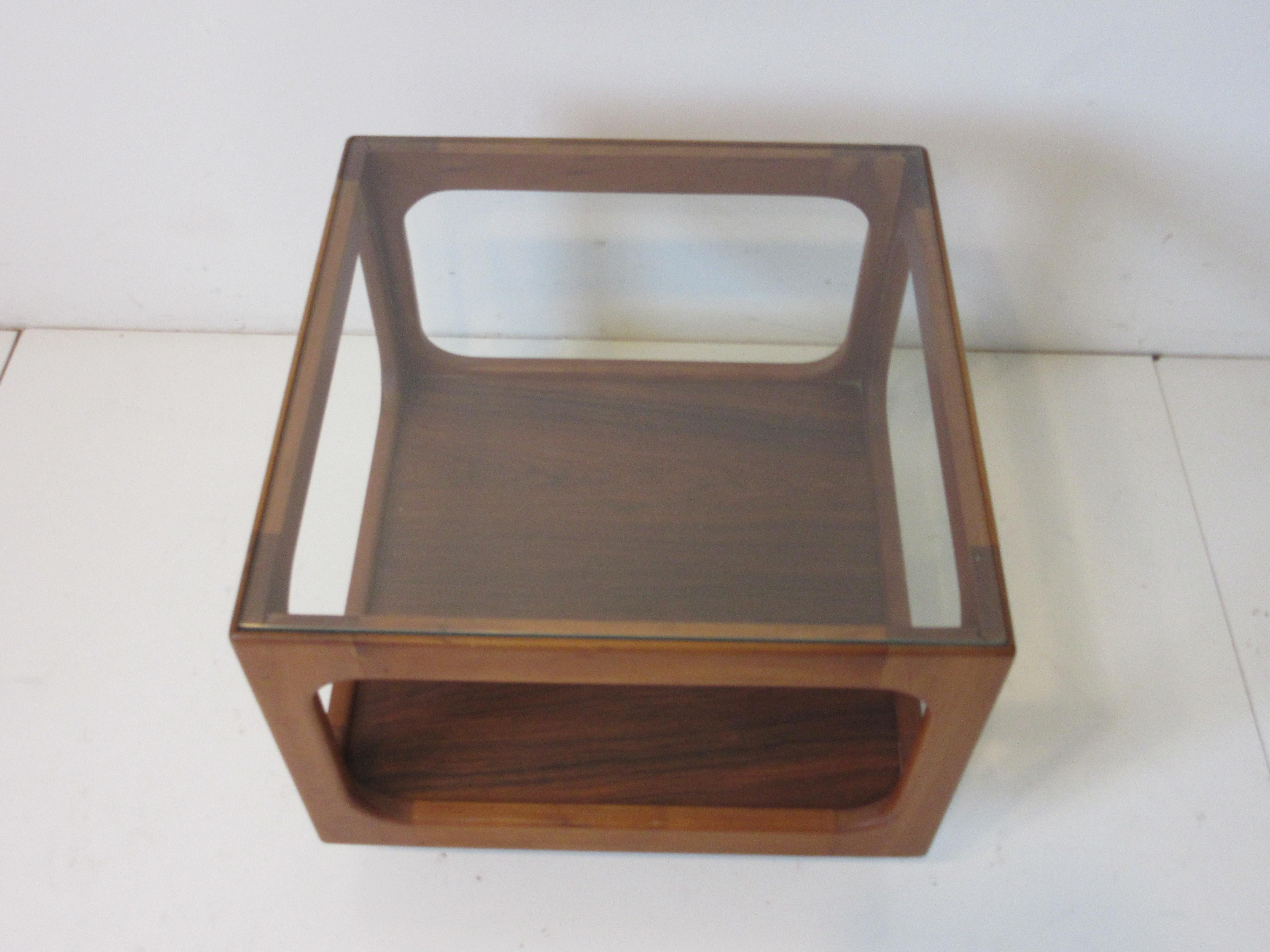 A walnut side table with open cube design having a inset tight fitting glass top in the manner of Otmar Danish styled furniture. The bottom of the cube has a darker walnut shelve base that the cube giving the piece some contrast with the kick