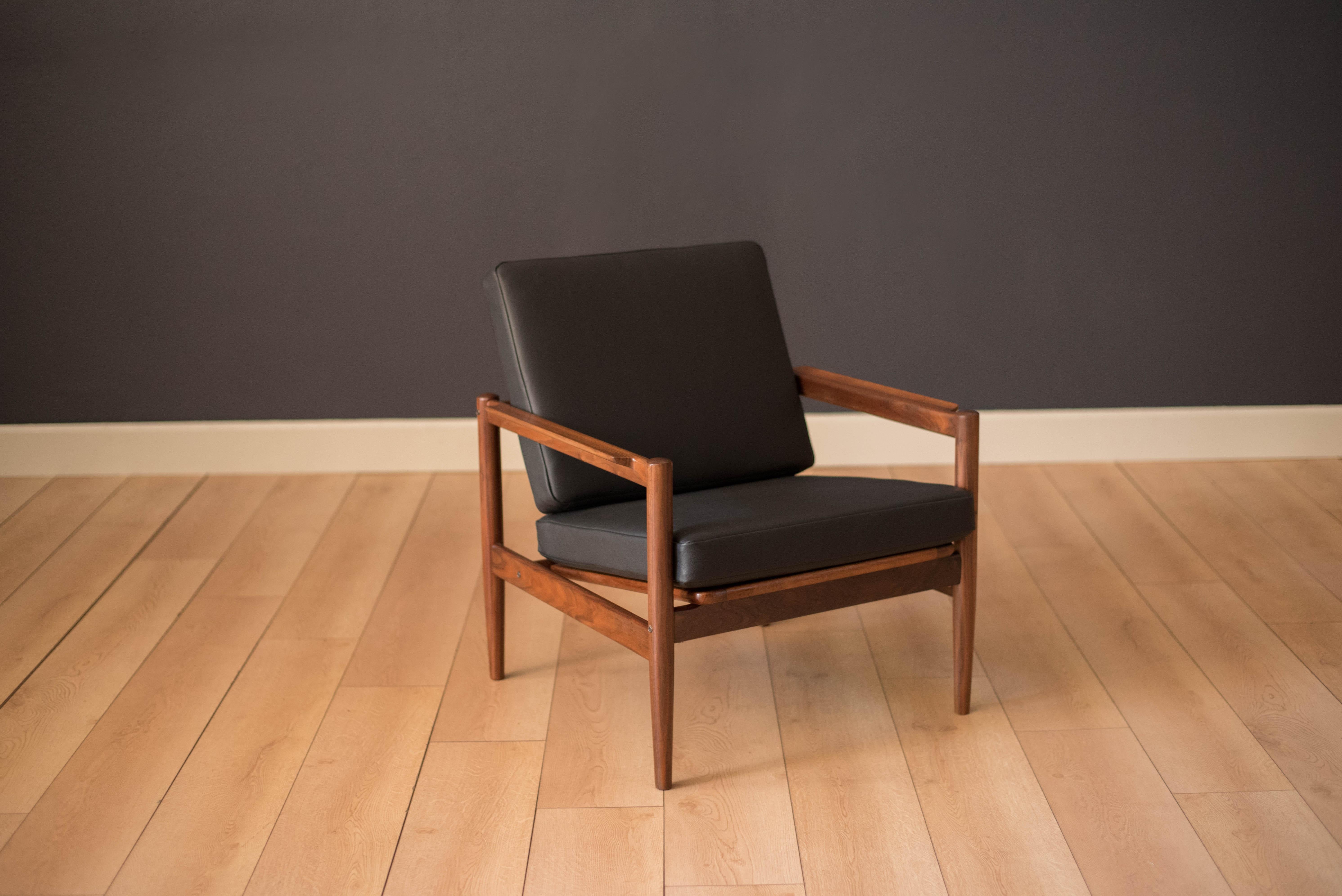 Vintage Danish lounge chair designed by Borge Jensen & Sonner for Bernstorffsminde Mobelfabrik. This lounge chair features a slatted backrest frame and sculpted walnut arms. Newly reupholstered in a matte black leather and includes two cushions.
