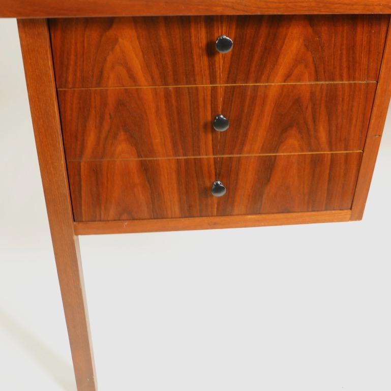 Very chic and stylish Mid Century desk in the Danish Modern style. This desk features a sculpted top having a raised wrap around edge, three drawers on left with 4 inch rosewood fronts, a center pencil drawer with a walnut front, and on the right, a