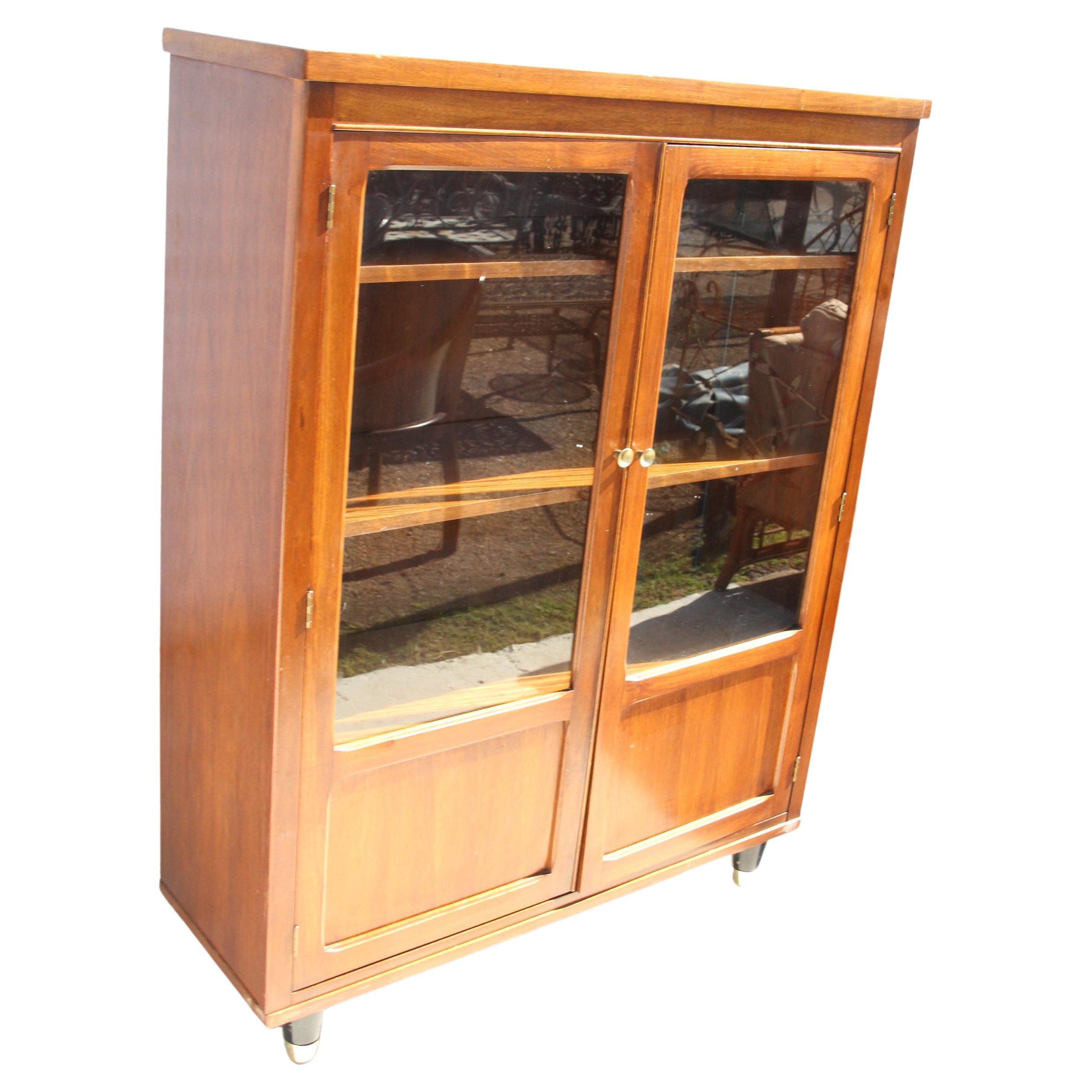 Midcentury Walnut Bookcase

Perfect for china, glass, bottles, books, etc. 
The cabinet has three shelves that can be placed in different positions 

The doors have integrated handles and the cabinet stands on tapered legs with brass caps. Brass