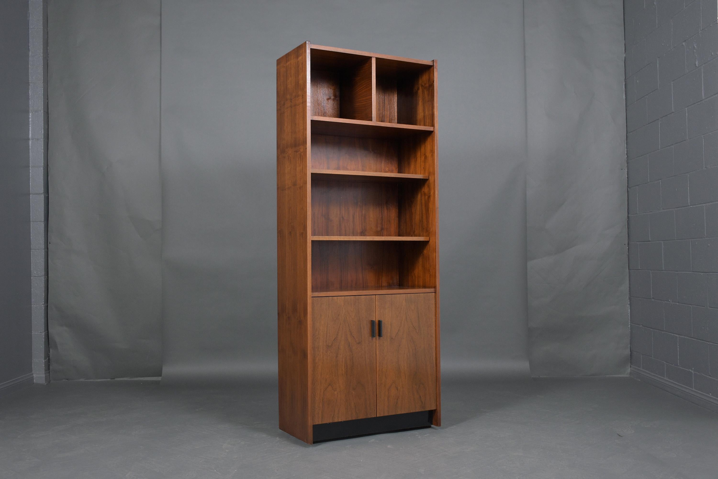 An extraordinary vintage mid-century modern bookcase is crafted out of walnut wood and has been professionally restored by our team of in-house craftsmen. This wall unit features two cubbies and two open shelves on the top half and the bottom comes
