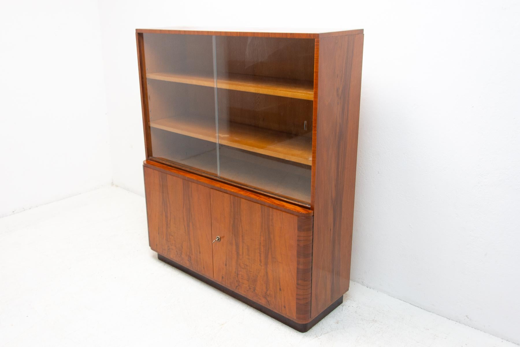 Mid-century walnut bookcase from the 1950's. It was made in the former Czechoslovakia in UP Závody company. Features a simple design, a glazed section with three storage spaces and two lockable at the bottom. In Very good condition. Beautiful walnut