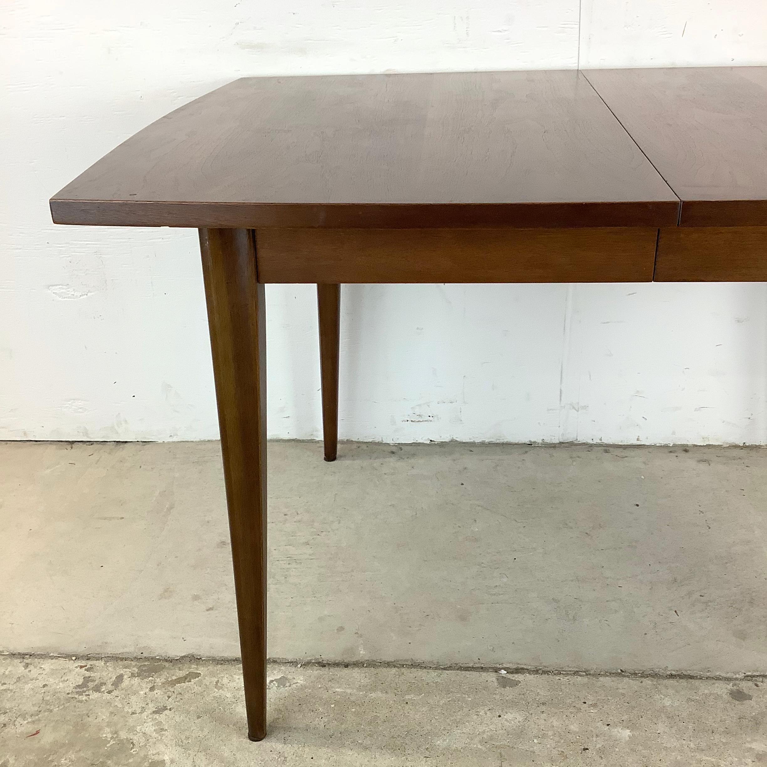 Elevate your dining experience with this charming Mid-Century Walnut Dining Table, a true gem of vintage craftsmanship. Designed with a removable leaf, this petite-sized table effortlessly transitions from intimate gatherings to larger dinners,