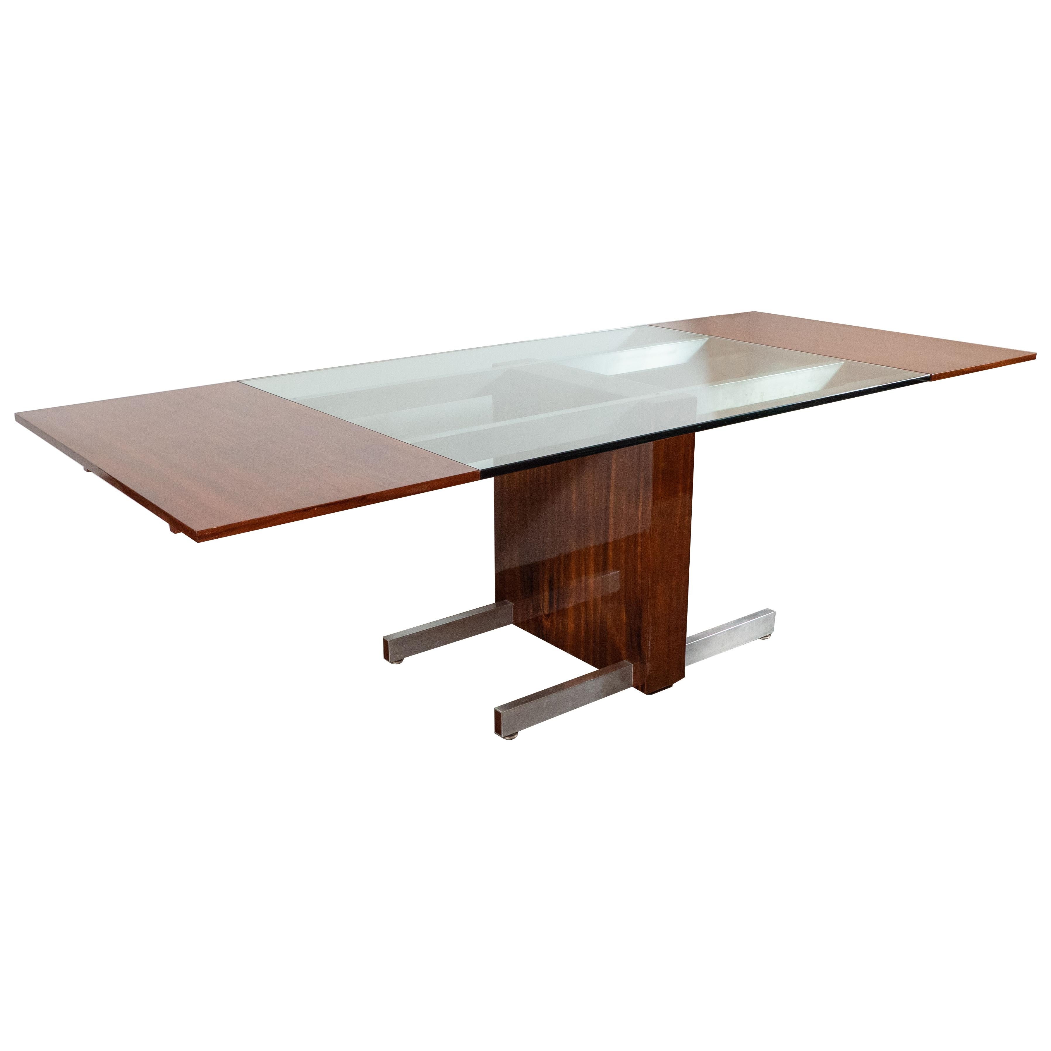This graphic and iconic dining/ console table was realized by the inimitable Vladimir Kagan, in the United States, circa 1970. It features a rectangular top with a glass center framed by two bookmatched walnut ends. The top is supported by a solid