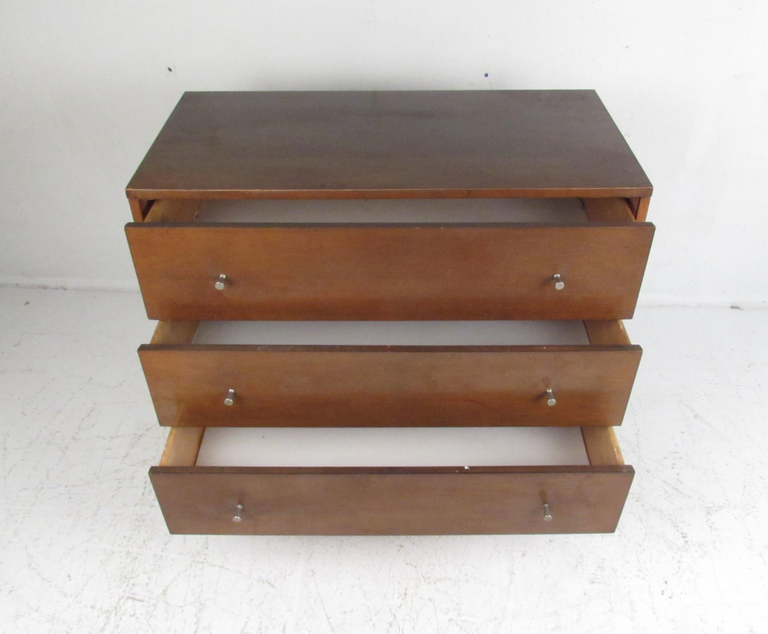 This beautiful vintage modern chest features three large drawers with metal conical pulls on each. Straight line midcentury design with tapered legs and a vintage walnut finish. This stylish dresser makes the perfect addition to any modern interior.