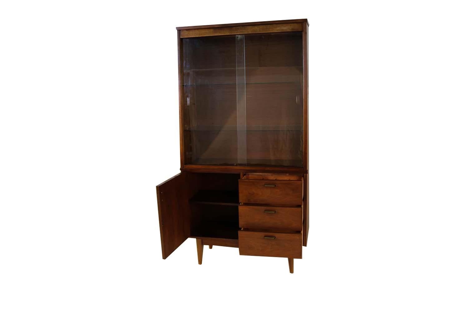 Vintage midcentury walnut china cabinet by Stanley. This stunning china cabinet with its clean unadorned style is a beautiful example of Danish modern furniture. The lighted cabinet features an upper cabinet with sliding glass doors and a lower