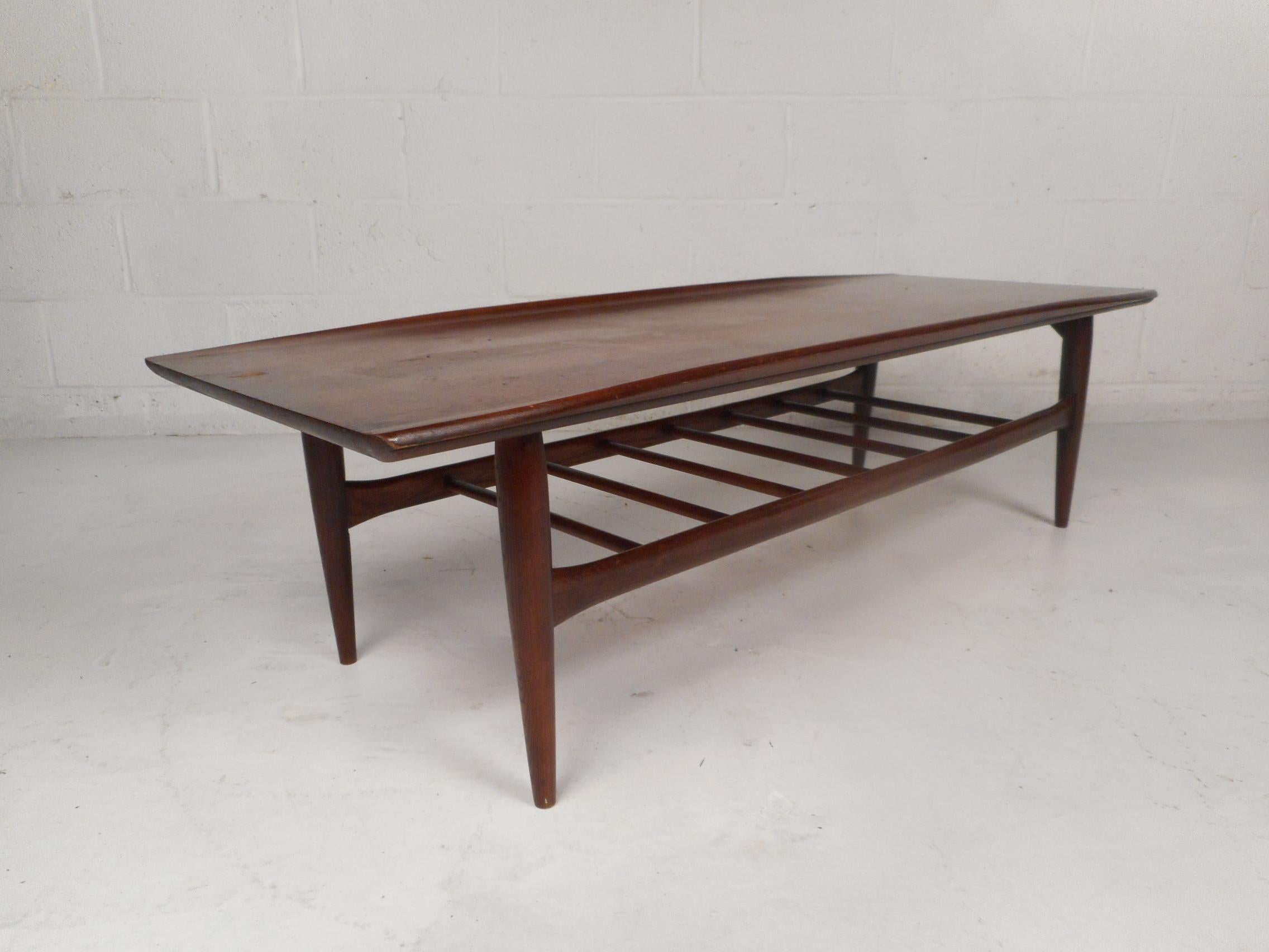 Stylish midcentury coffee table. Sleek design including accented raised edges along the tabletop, numerous stretchers spanning the base, sculpted frame and tapered legs. Beautiful midcentury piece sure to please in any modern interior. Please
