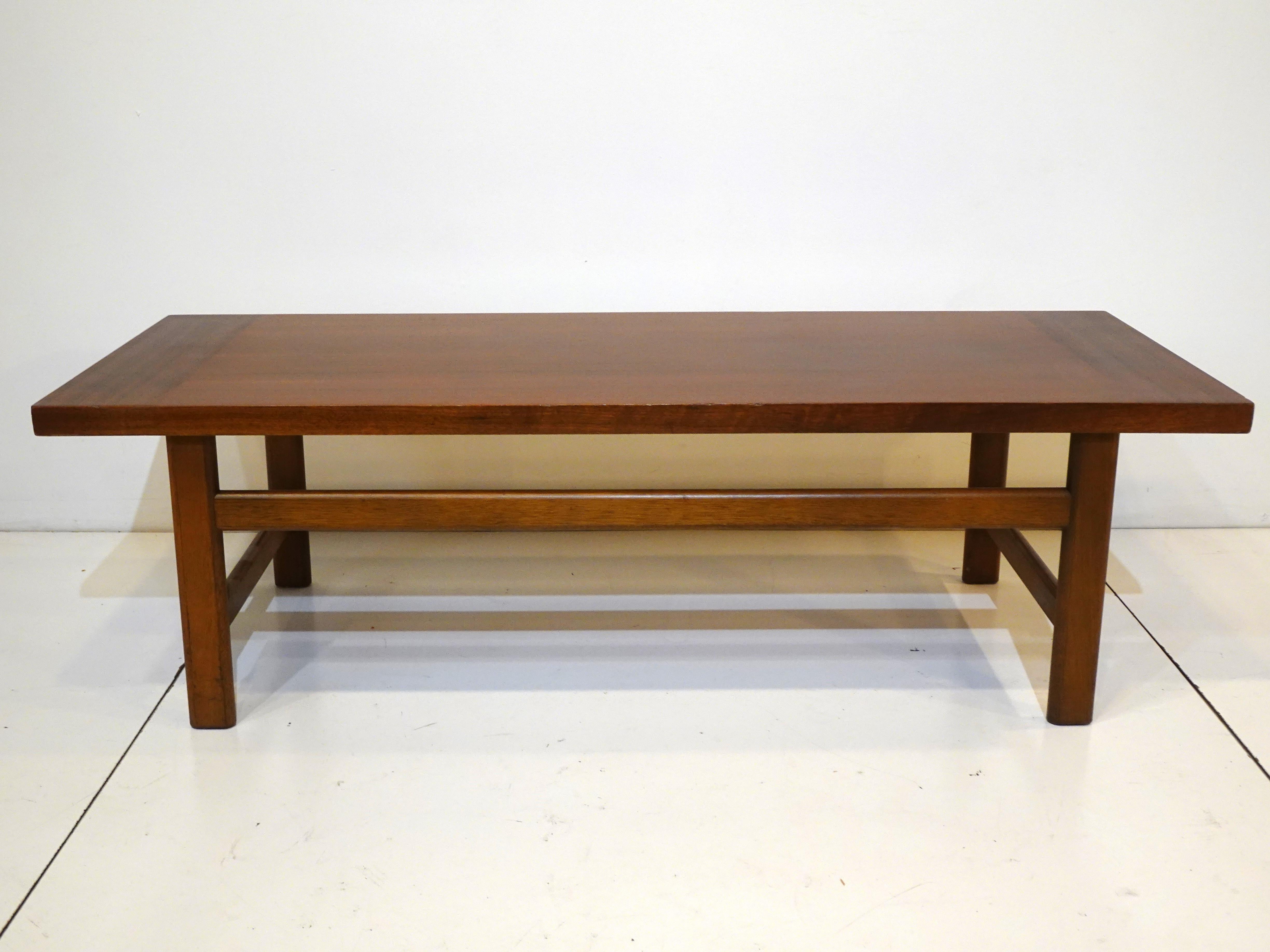 A well constructed walnut mid century coffee table in the manner of Harvey Probber with nice contrasting graining to each end. Having design detailed stretchers to each leg giving the piece interest and making it's very sturdy.
