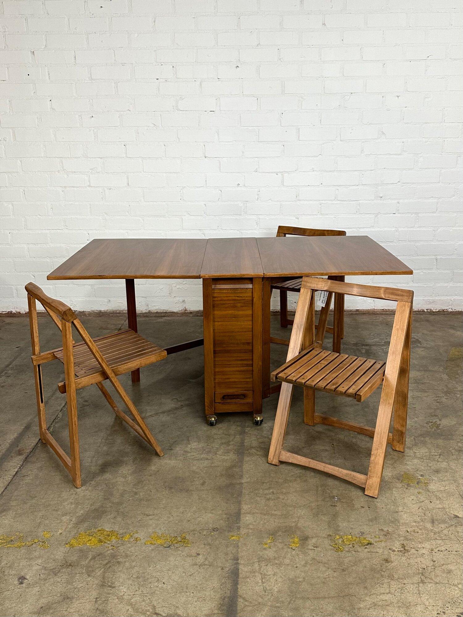 W62 D34 H29 KC28

Vintage walnut dining table with fold down leaf extensions, once down make the table slim and compact. The table features a Tambour slot on the center to hide folding chairs, available in separate post. The table has been fully