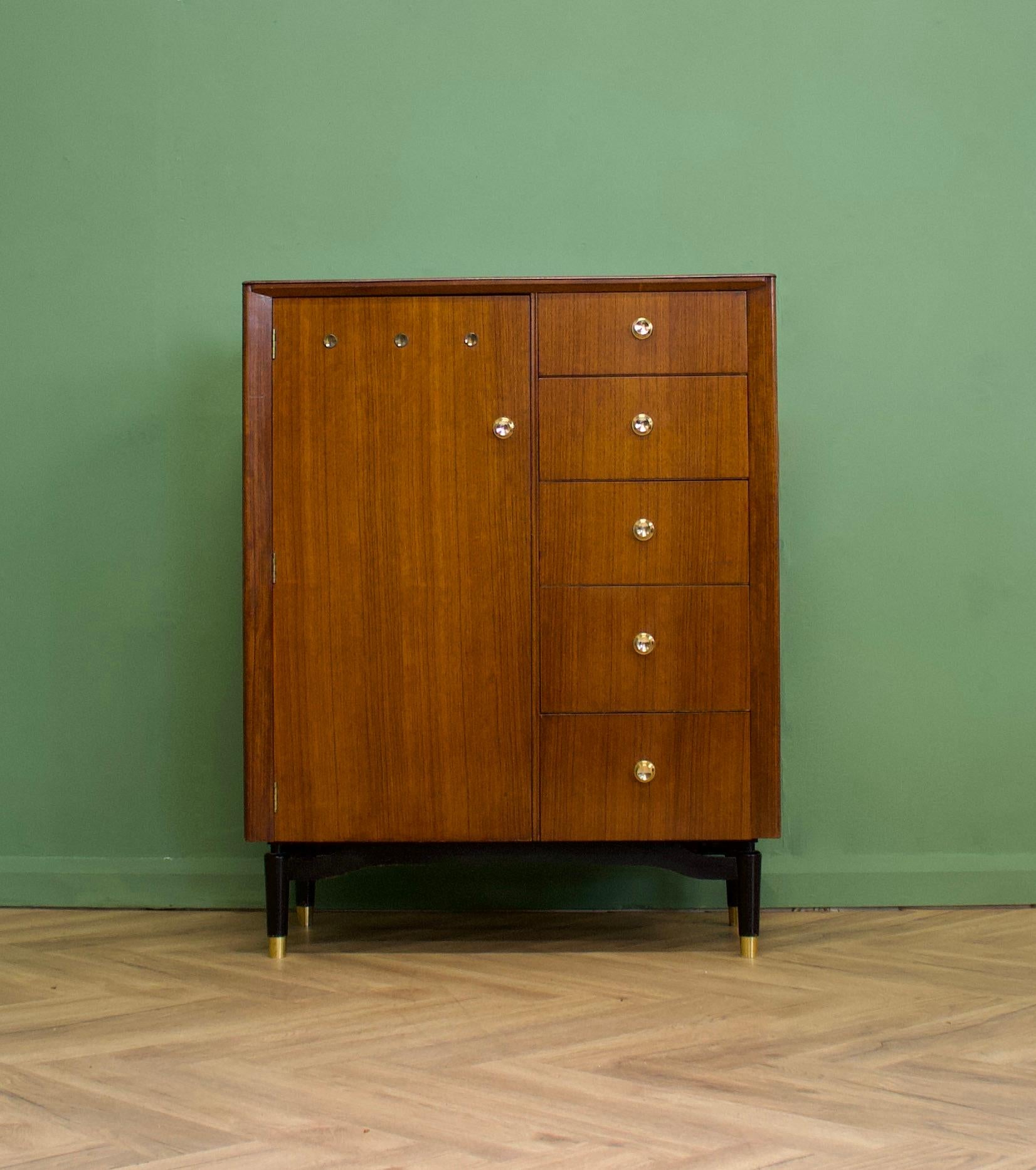 A beautiful quality walnut compact wardrobe/compactum from CWS, circa 1950s
The piece features a hanging rail compartment and five drawers to the right hand side - standing on ebonised legs with brass cup feet - the handles are also solid brass


 