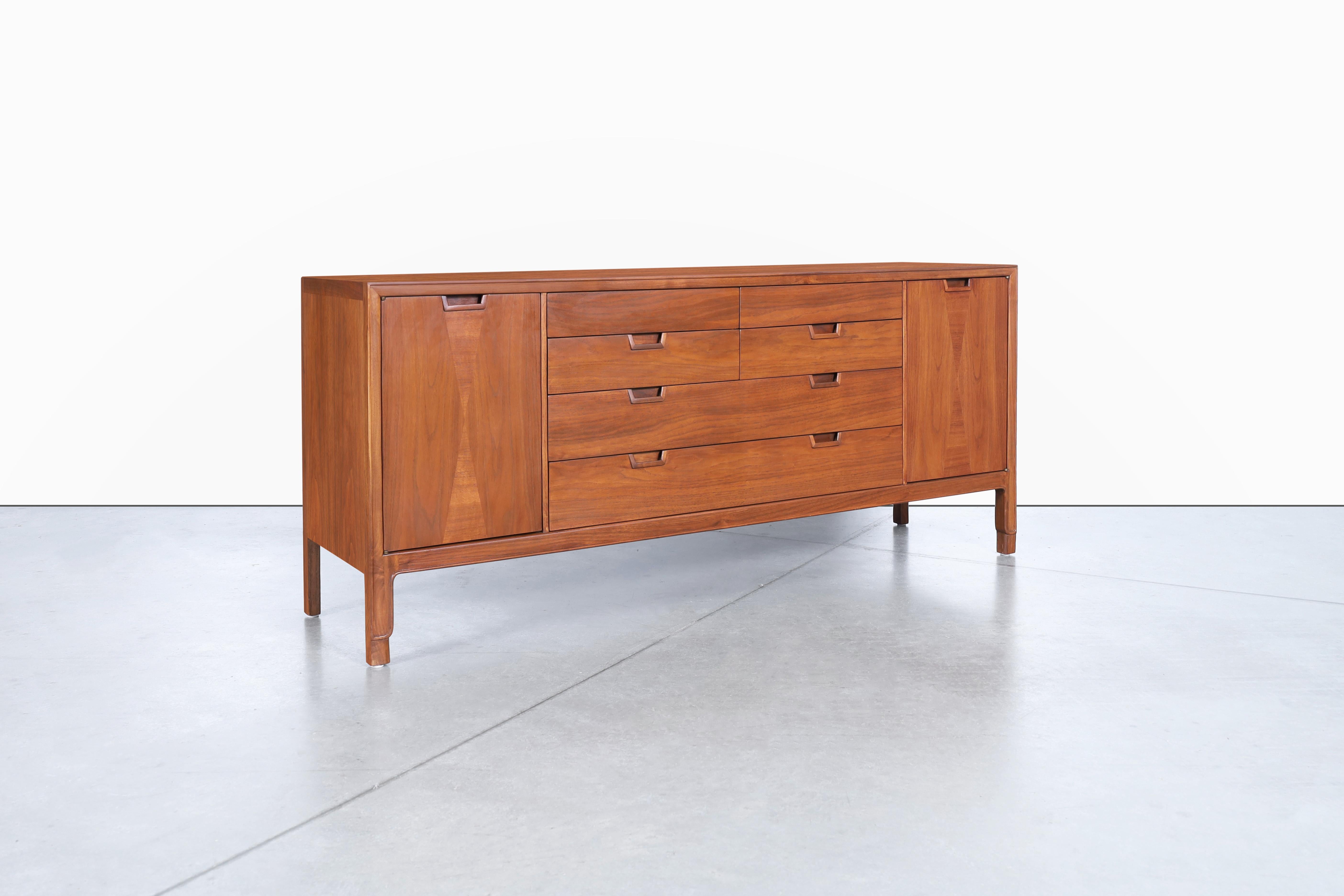 This stunning mid-century walnut credenza is a timeless piece manufactured by John Stuart Inc. from Mount Airy, North Carolina in the 1960s. It's part of the esteemed Janus Collection renowned for its highest quality pieces. The credenza features a