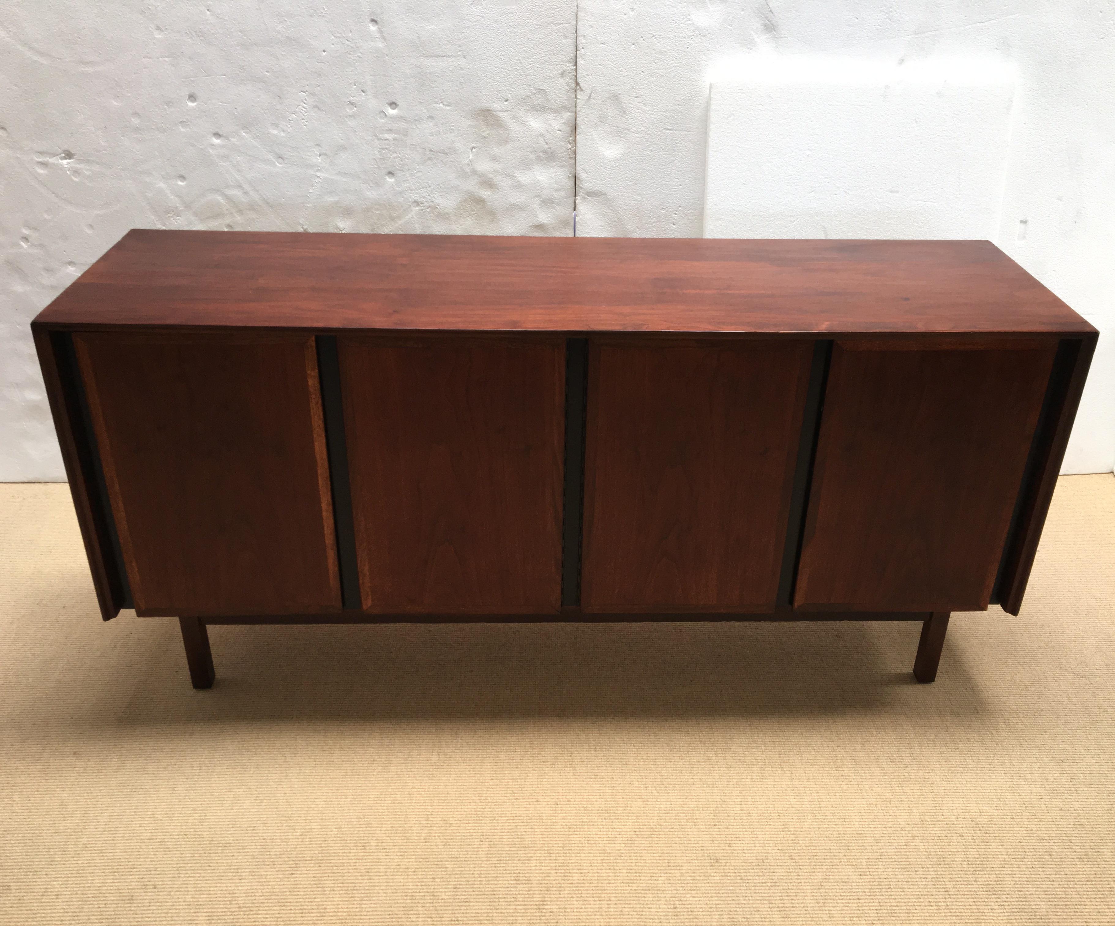 A walnut dual cabinet credenza with white lacquered drawers on the left and storage space/shelving on the right.
Branded Dillingham sticker rests inside the top drawer.