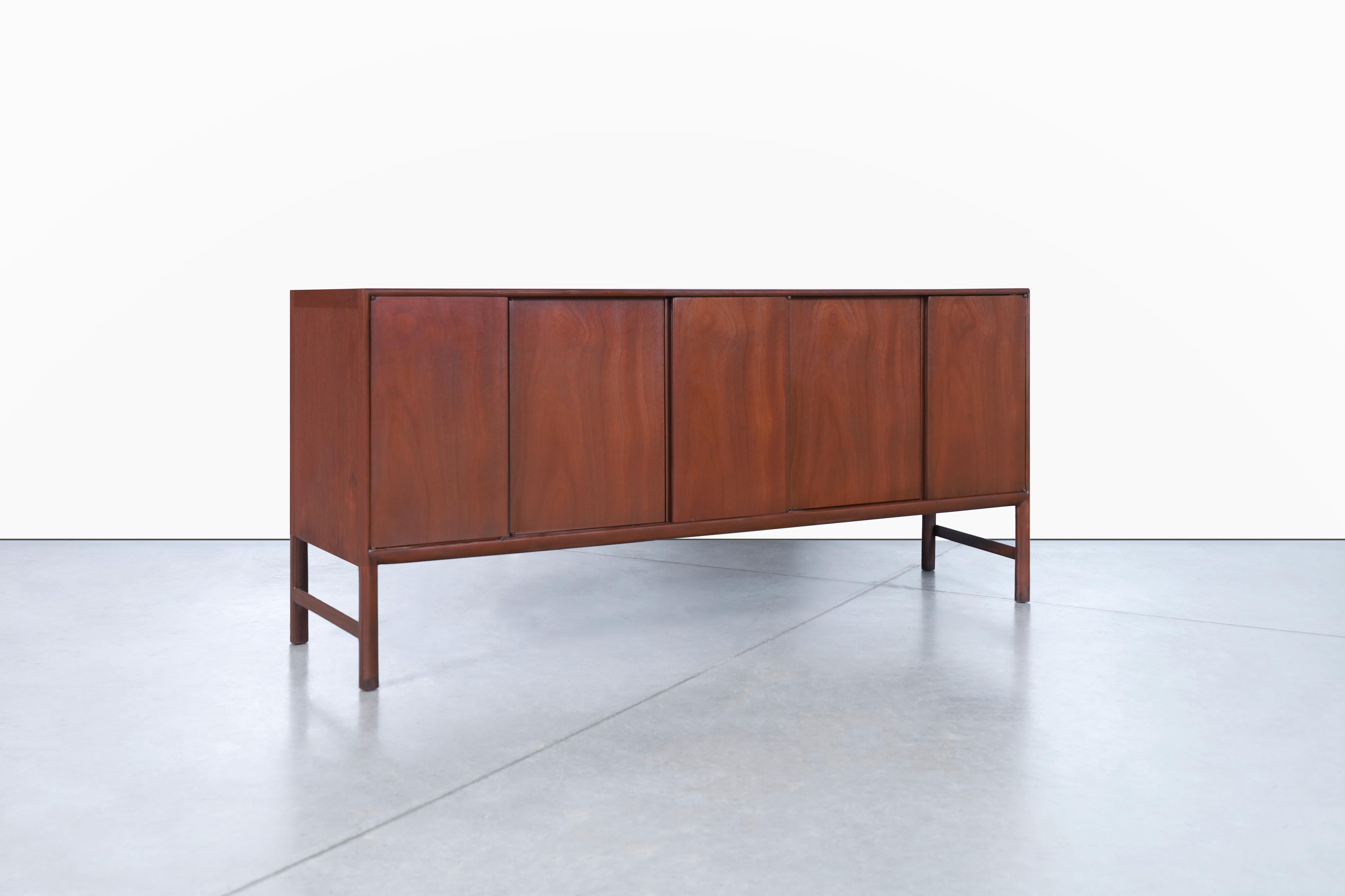 Mid-century walnut credenza designed by Raymond Sobota for Mount Airy in the United States, circa 1960s. Behold the epitome of mid-century modern design - a perfect balance of form and function. This stunning credenza is expertly crafted from rich