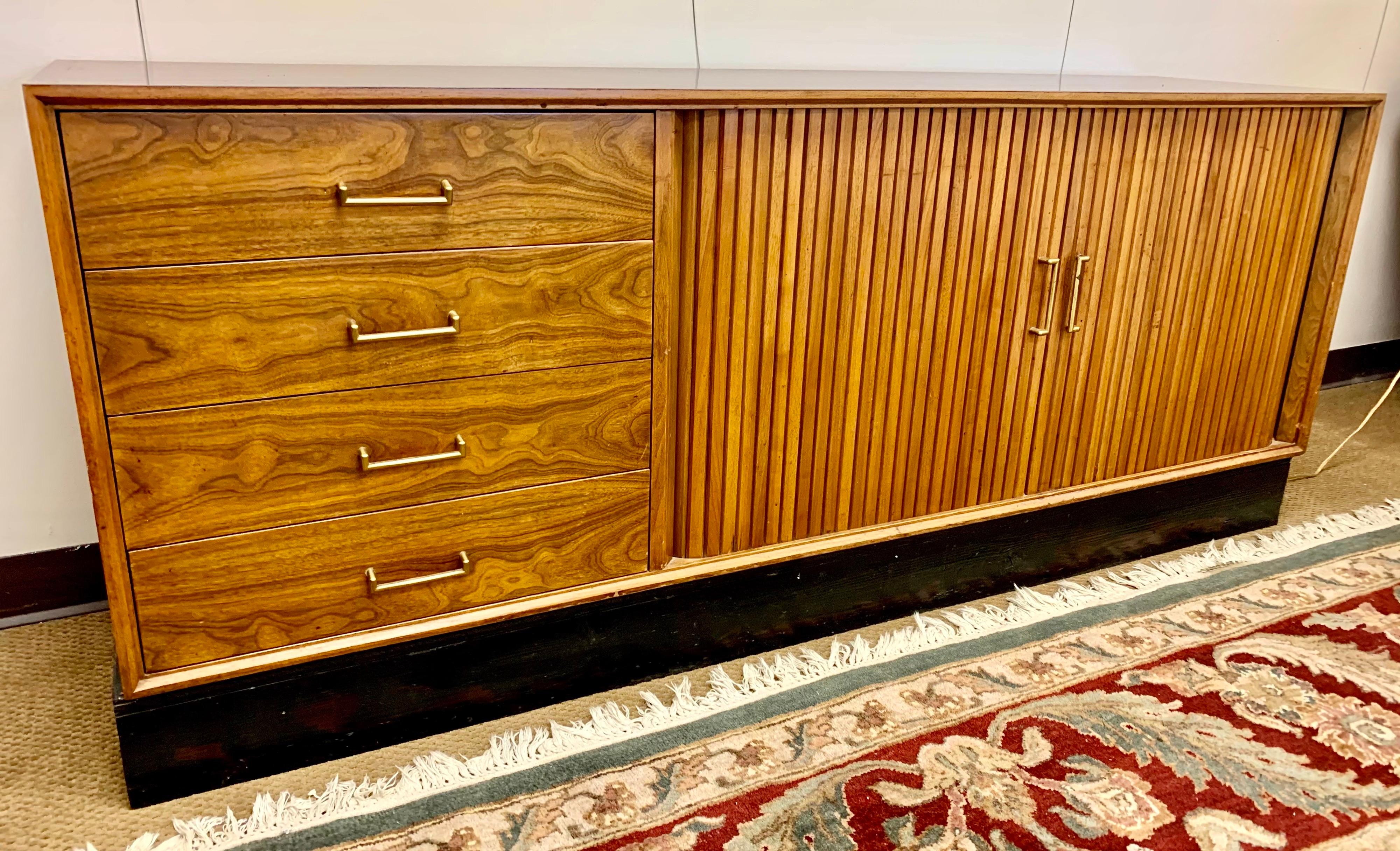 This versatile walnut mid-century credenza can be used as a sideboard, buffet, dresser or entertainment console. It has plenty of storage and features two tambour doors that open to shelves and four large drawers. It rests on a black wooden plinth.