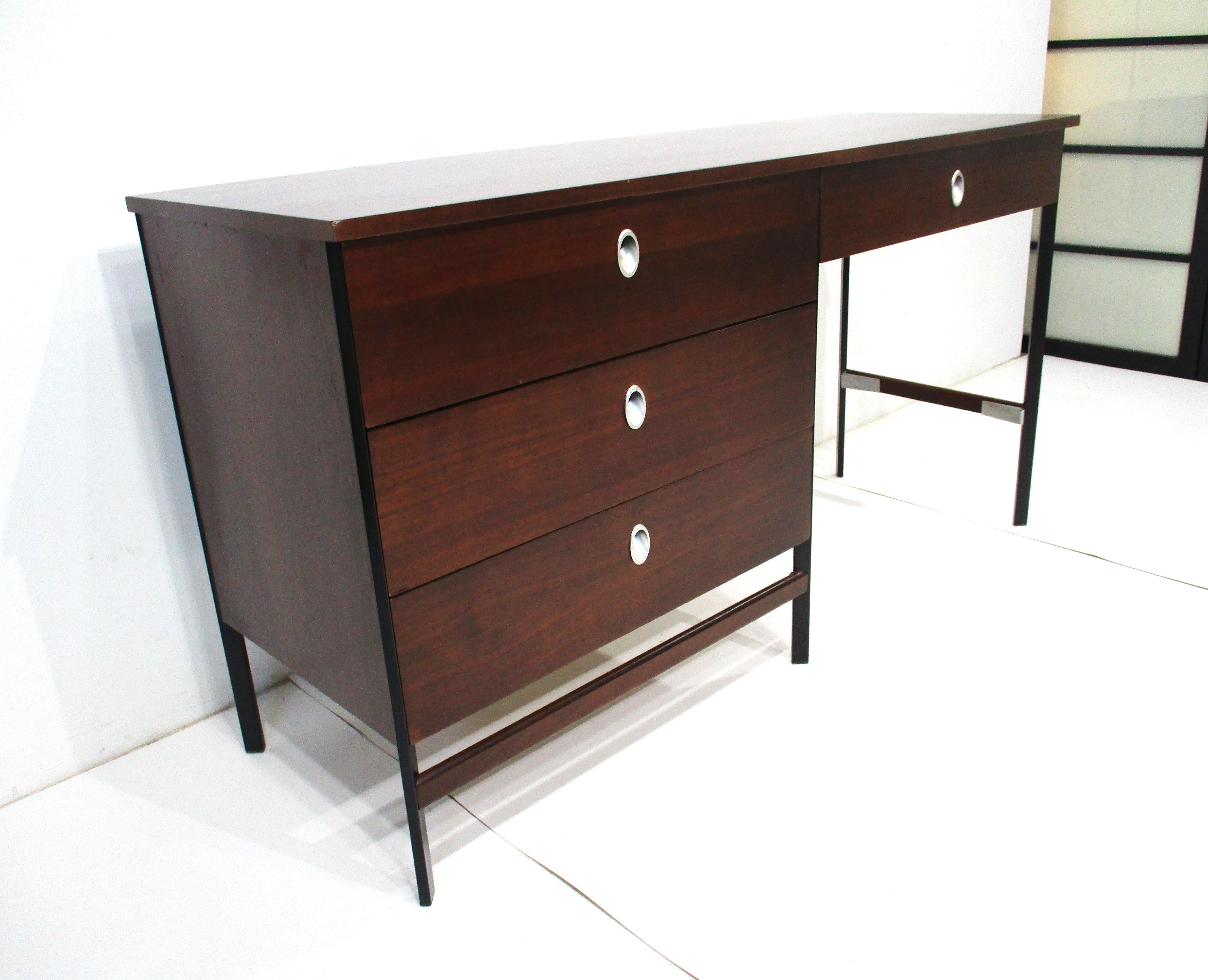 A dark walnut desk with three full sized side drawers and a smaller drawer in front of the chair area all with sculptural brushed aluminum pulls . The satin black frame gives the piece a rich modern look which after 60 years is still fresh .