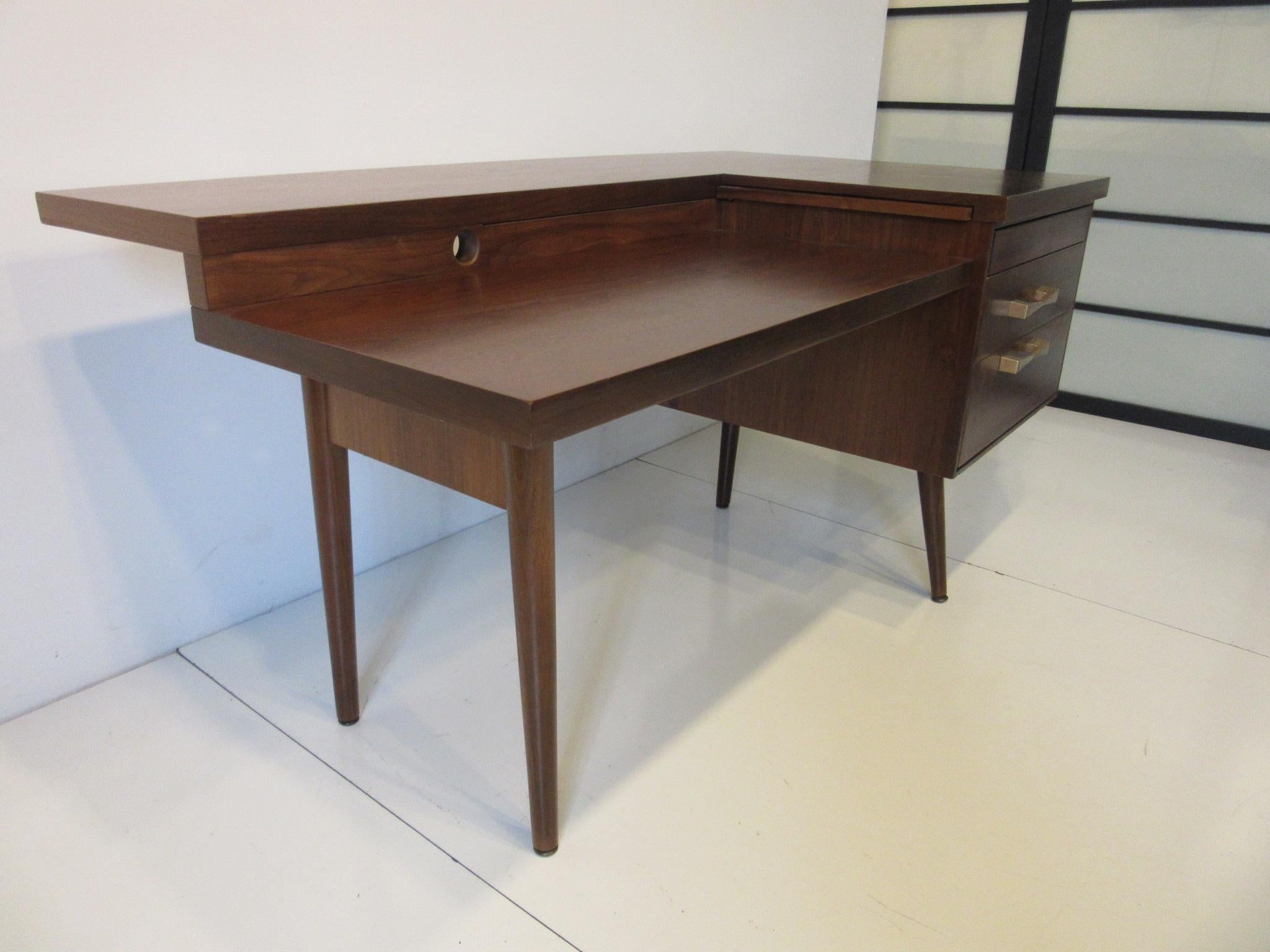 A very versatile walnut desk which is the right size for home or office with two drawers having great bow tie styled brass pulls and long strong conical legs . Making this desk perfect is a two tiered desk top with pull out height extension which