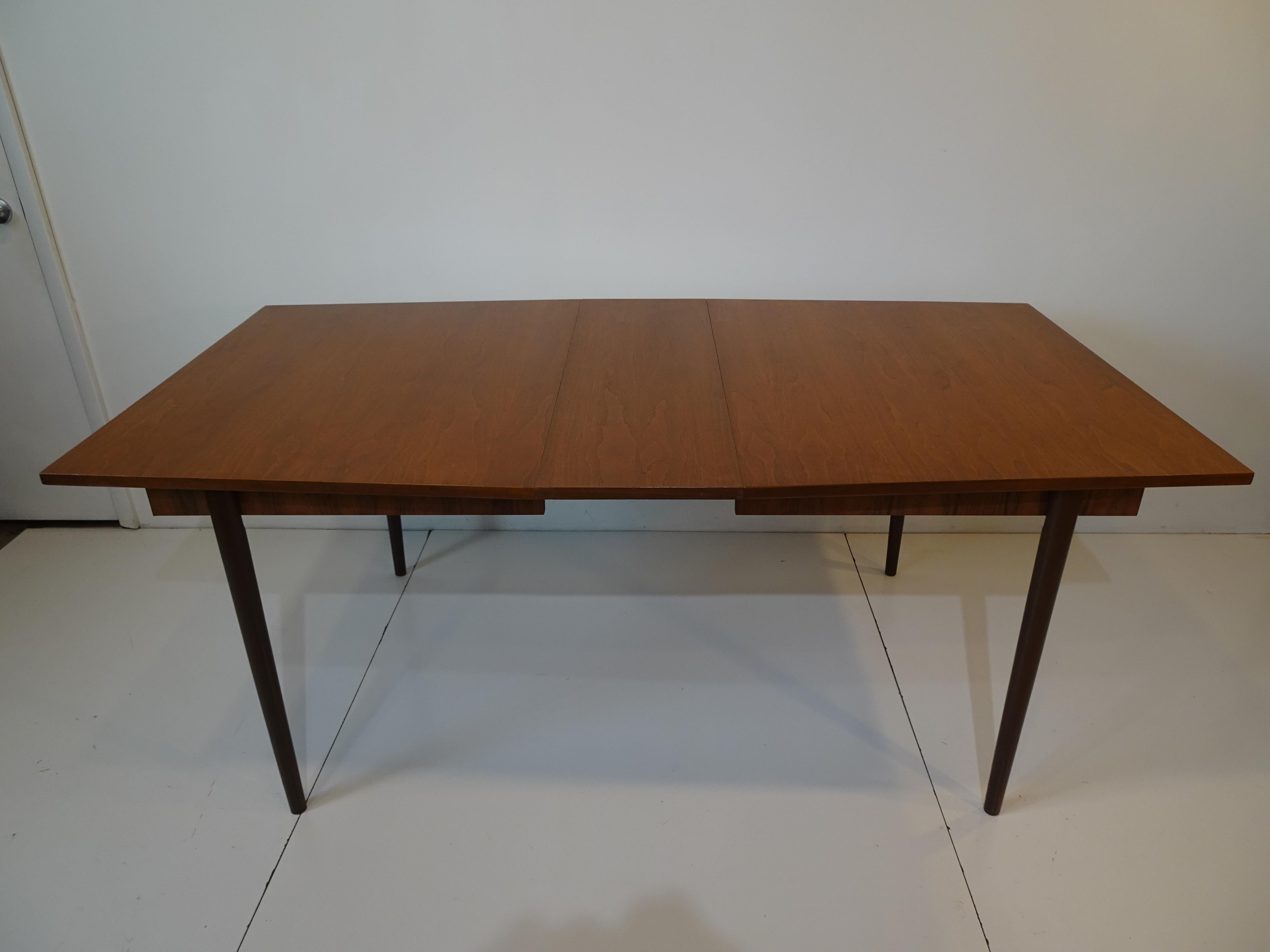 A medium toned mid century walnut dining table with tapered ends and one 12