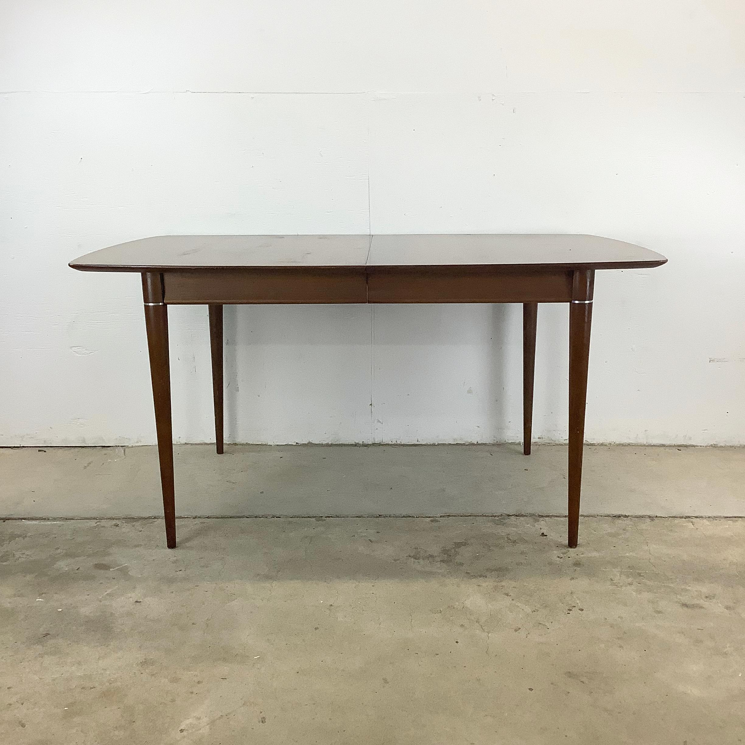 This mid-century dining table with a removable leaf and tapered walnut legs offers the perfect blend of form and function for your dining space. Featuring a classic walnut finish and unique modern metal band trim, this table exudes mid-century