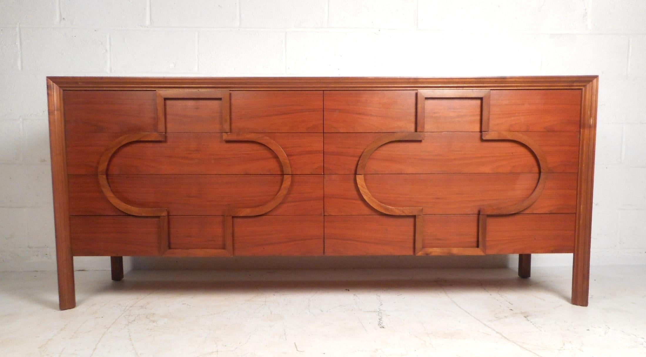 This wonderful vintage dresser has a unique embossed design that is not only stylish, but also practical as the pattern doubles for drawer pulls. The dresser has a brilliant walnut finish and eight spacious drawers. Designed by Edmund Spence, this