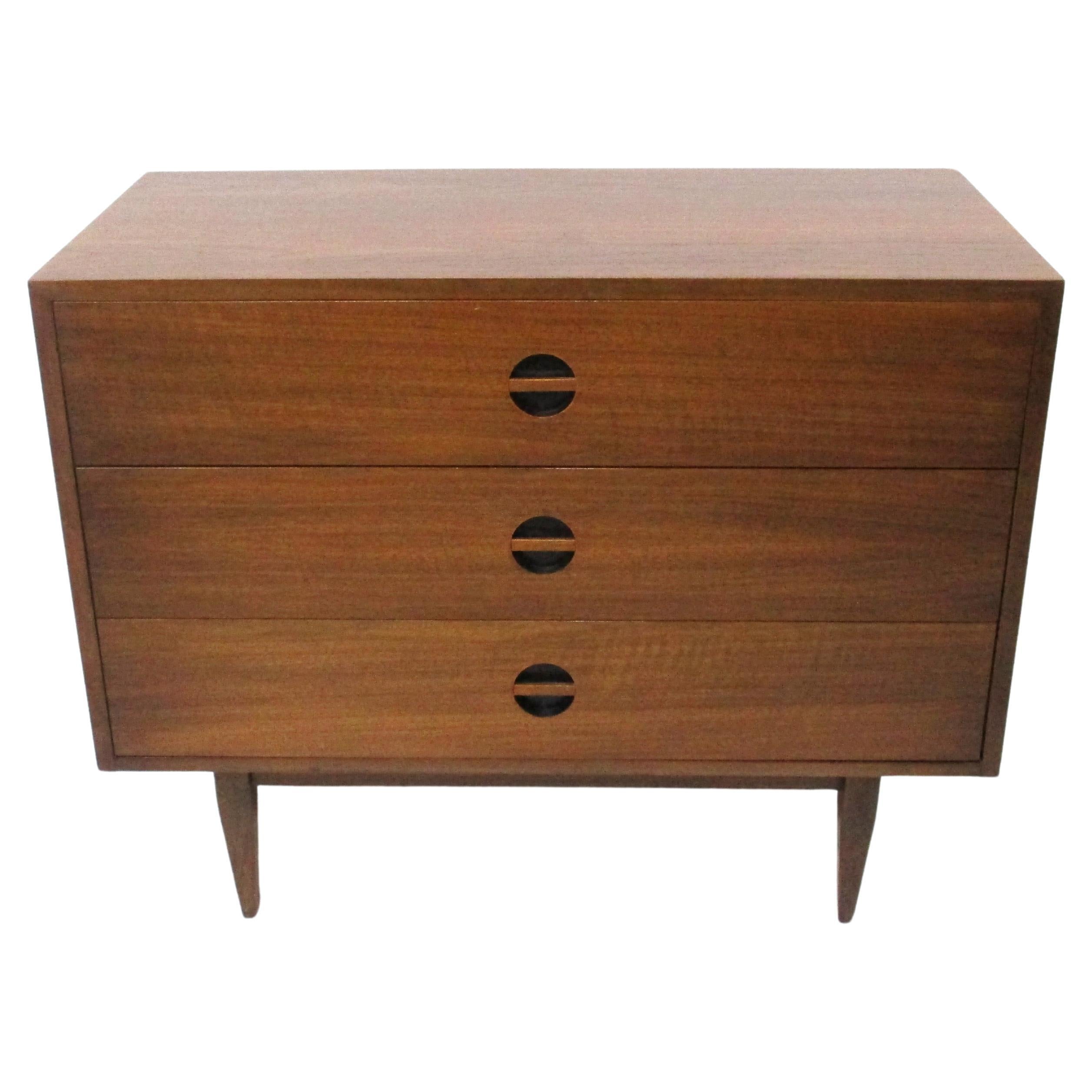 A nicely grained medium dark walnut three drawer dresser with cut in pulls having satin black back rounds sitting on tapered legs . Designed in the manner of Arne Vodder and manufactured by the West Michigan Furniture company from an area that was