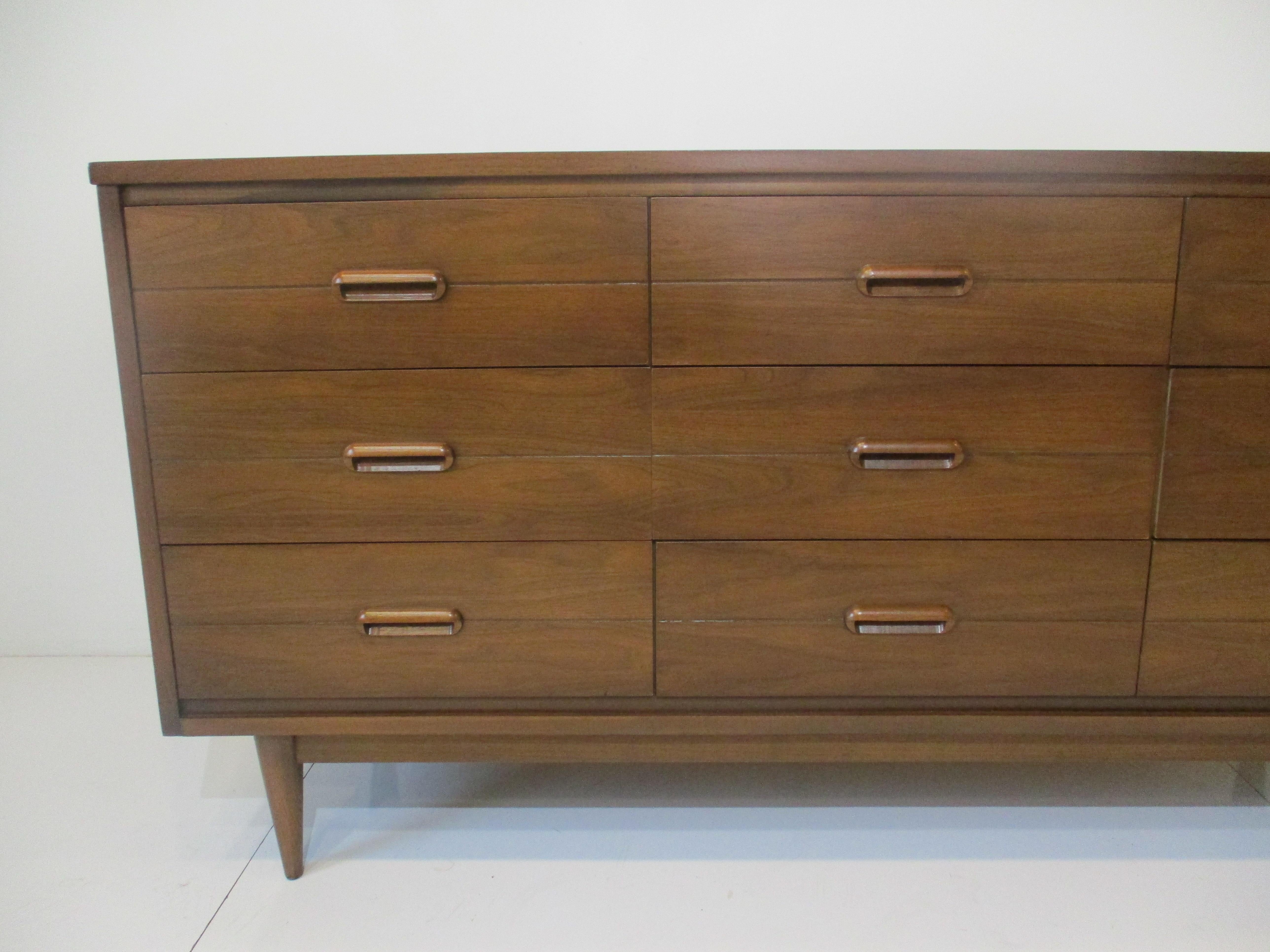 A walnut nine drawer Mid-Century Modern dresser with wooden pulls in the manner of Danish furniture. Each drawer has a dark line to the center making a nice detail with conical legs a nice simple design.