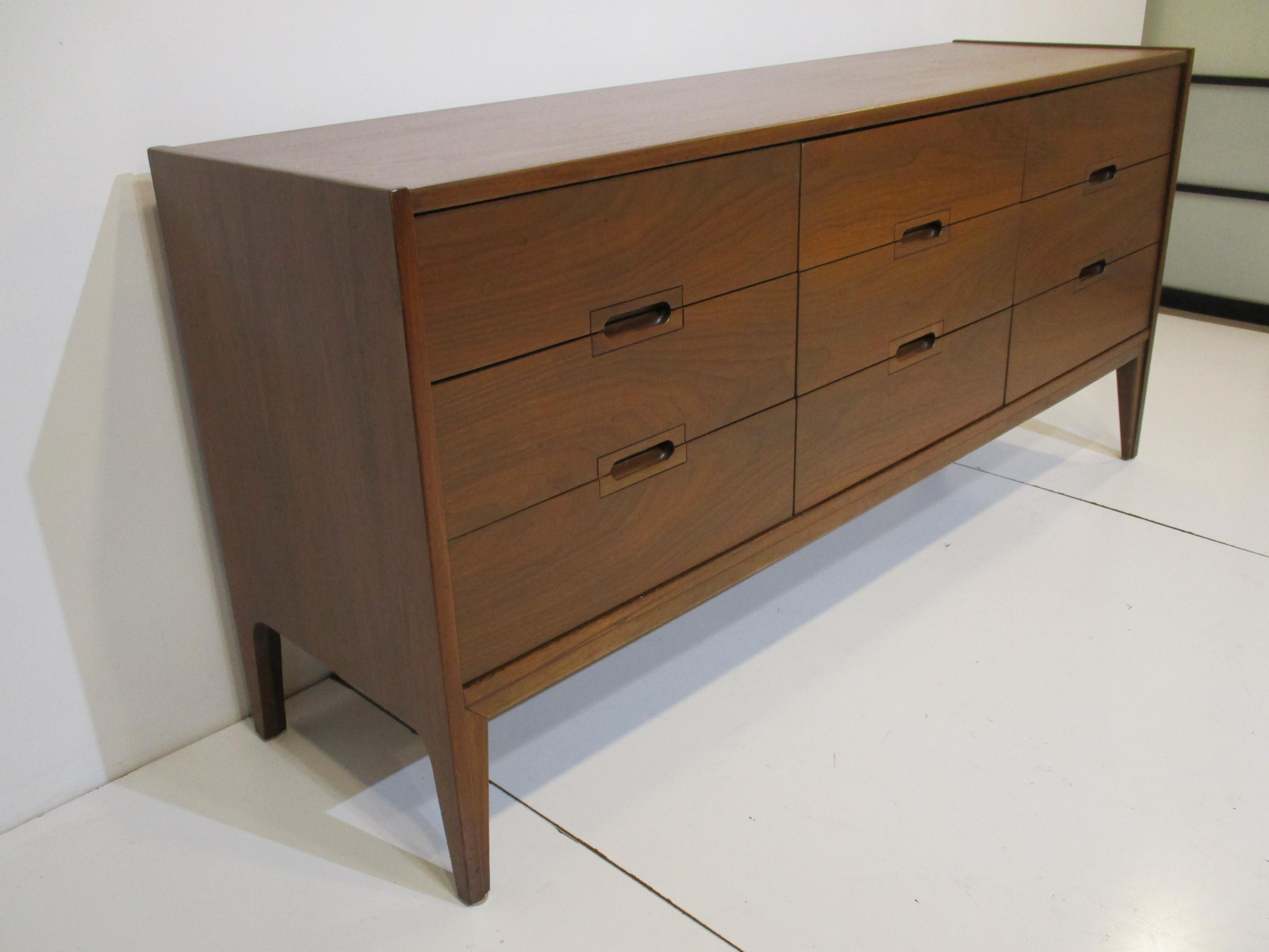 A very well grained medium dark walnut nine drawer dresser chest with flush pulls making the piece very clean and tidy. The spear styled legs have a nice cut in line detail that goes into the bottom stretcher across the frame tying the form