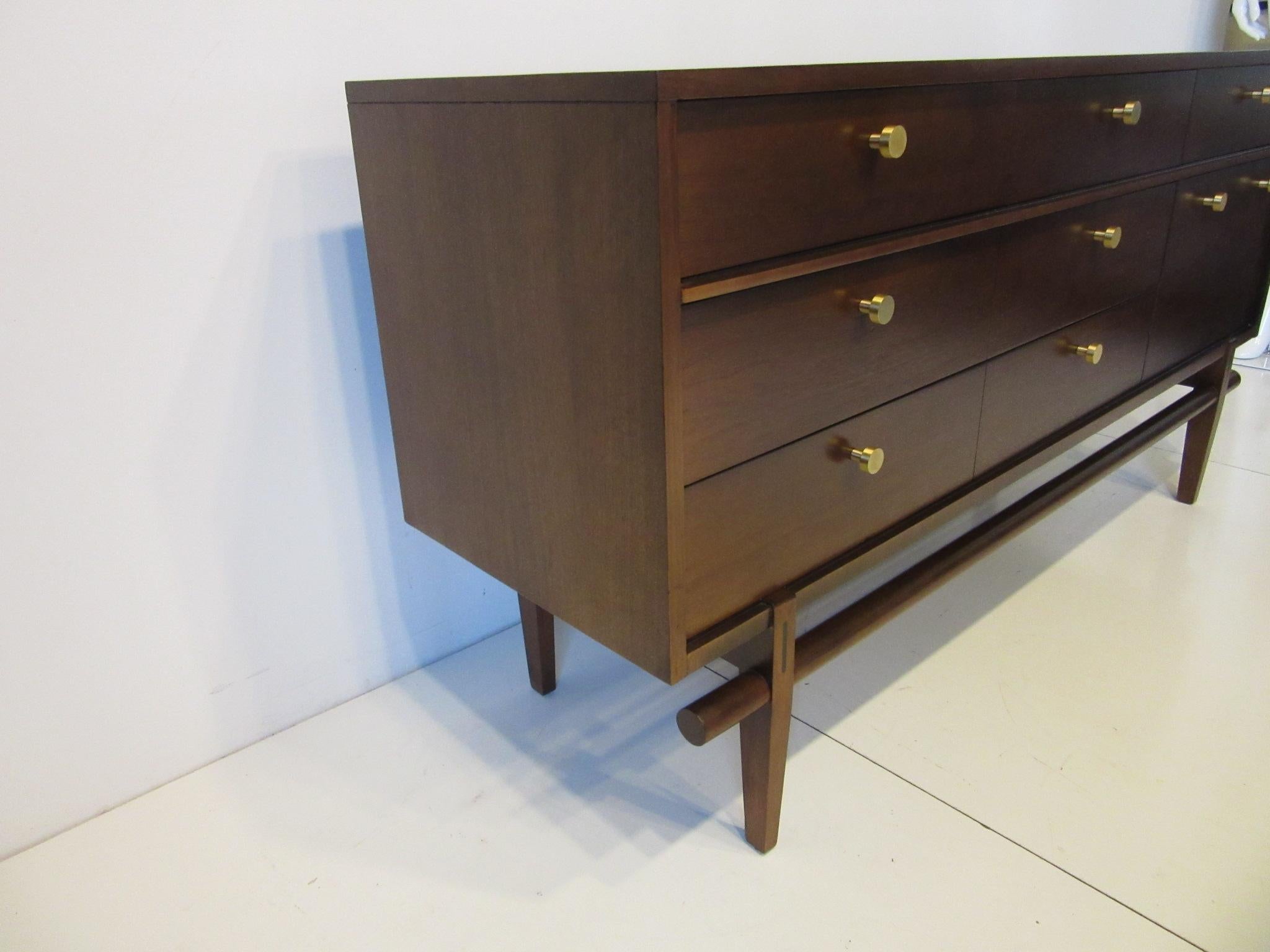 A medium toned walnut finished dresser / chest with six drawers, two full sized, three single and one larger drawer having heavy brass pulls. There's a darker wood inset to the upper leg and rounded stretcher design giving this piece an outstanding