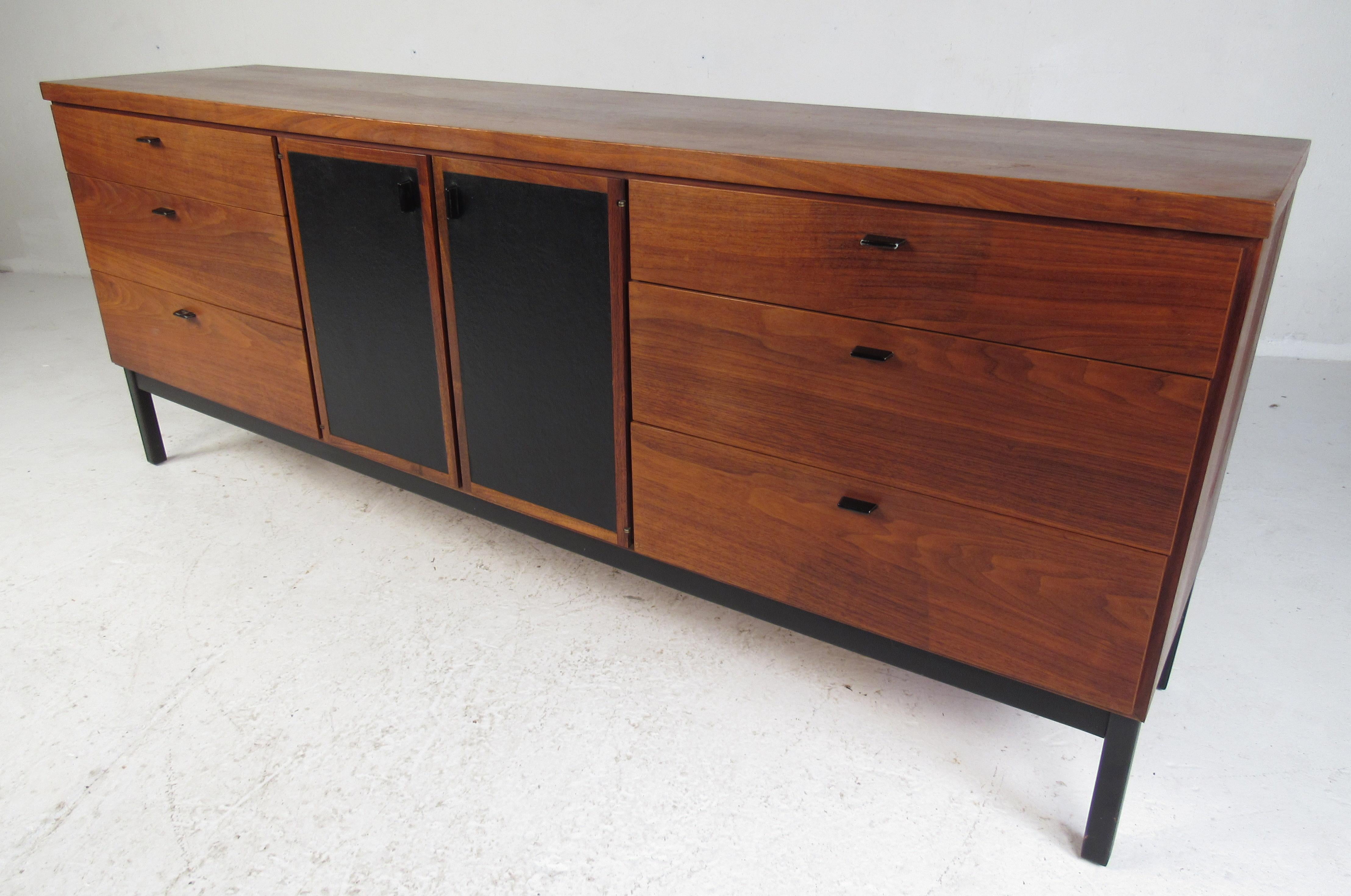A stunning vintage modern dresser that features two cabinet doors with leather fronts in the center. A sleek two-tone design with a black painted base, unusual drawer pulls and a vintage walnut finish. This beautiful midcentury case piece offers