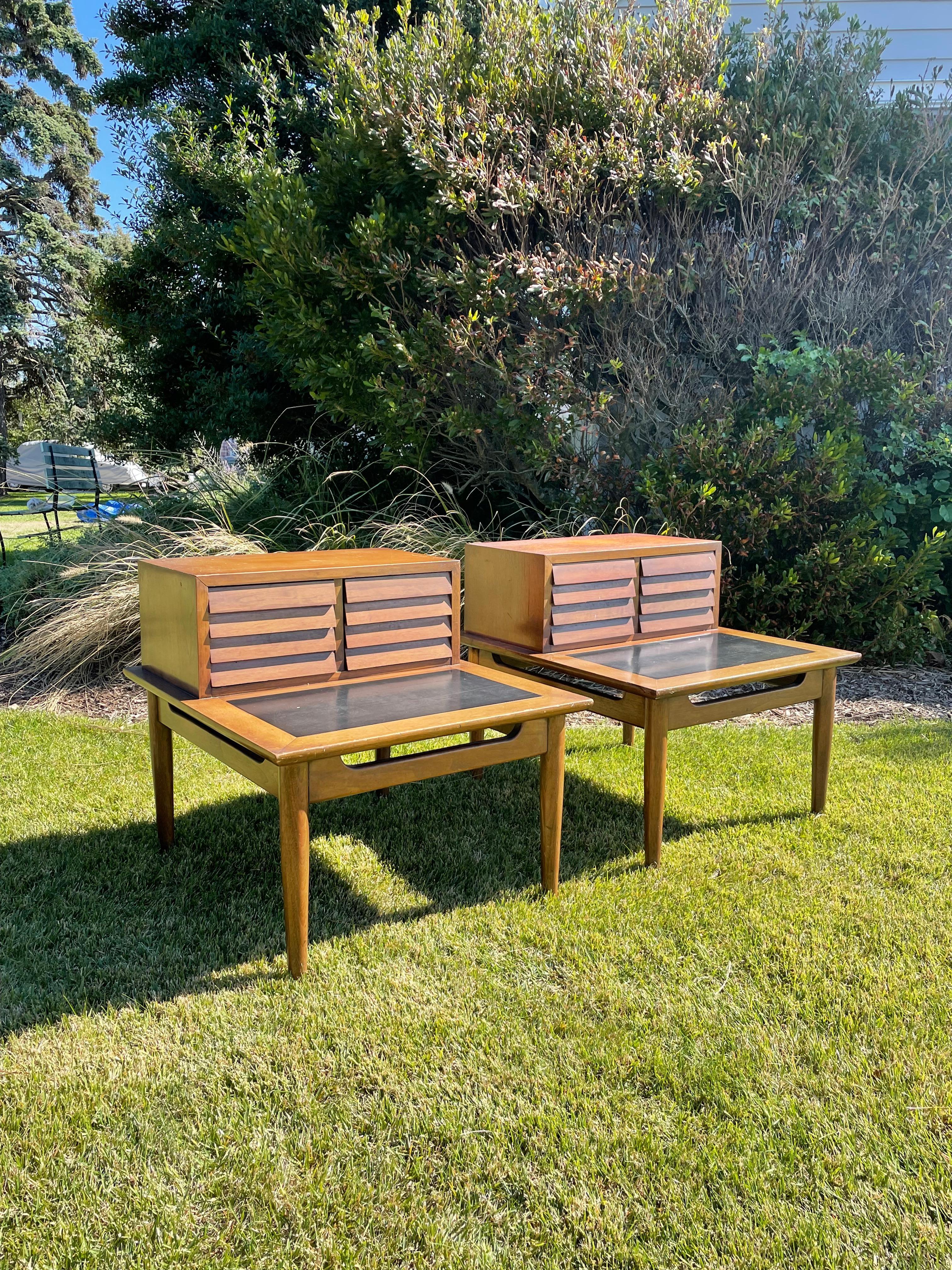 Handsome pair of architecturally designed two tiered end tables by Merton Gershun for American of Martinsville part of the “Dania” collection . The tables feature louvered deep dovetailed drawers, walnut frames, black tops and tapered legs. 1950s