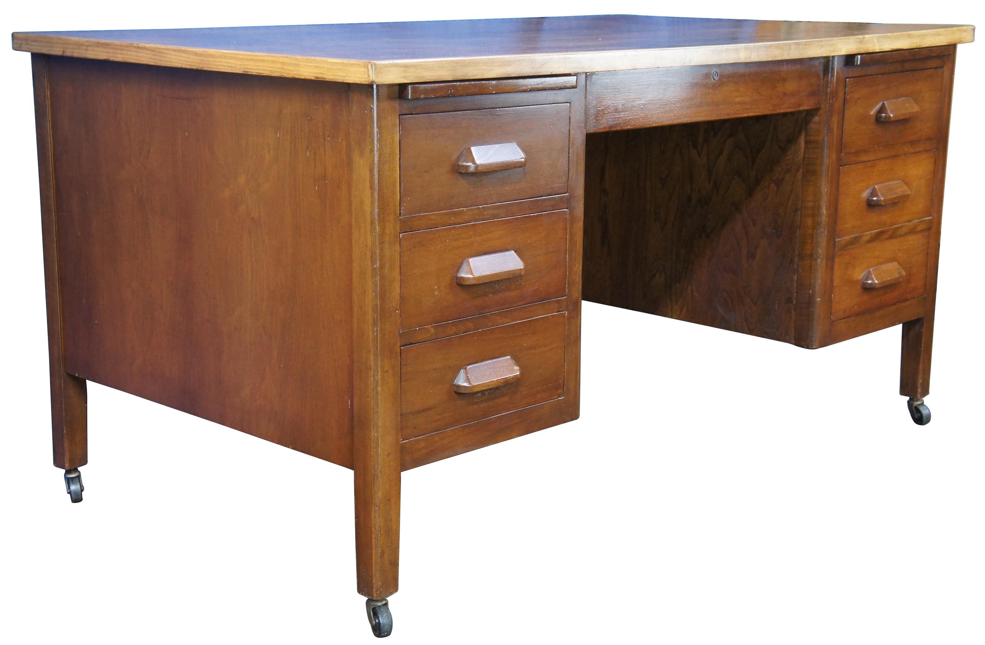 1940s vintage executive office / library / school writing desk. Made of walnut featuring rectangular form with six drawers, with two pull outs work surfaces and rolling casters. The central drawer includes a pencil insert. 

Measures: 34