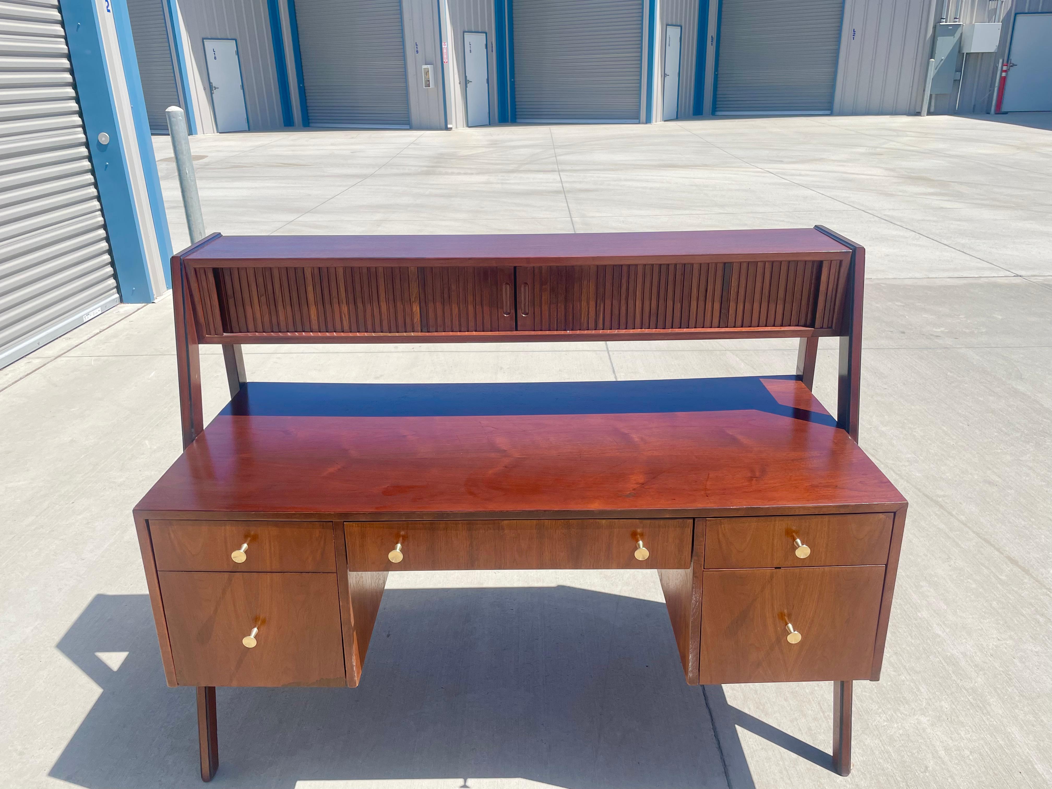 midcentury walnut floating tambour desk manufactured in the United States, circa 1960s. This vintage desk features a beautiful walnut grain and floating leg connected to the top, giving it the illusion that the tambour door is floating right in