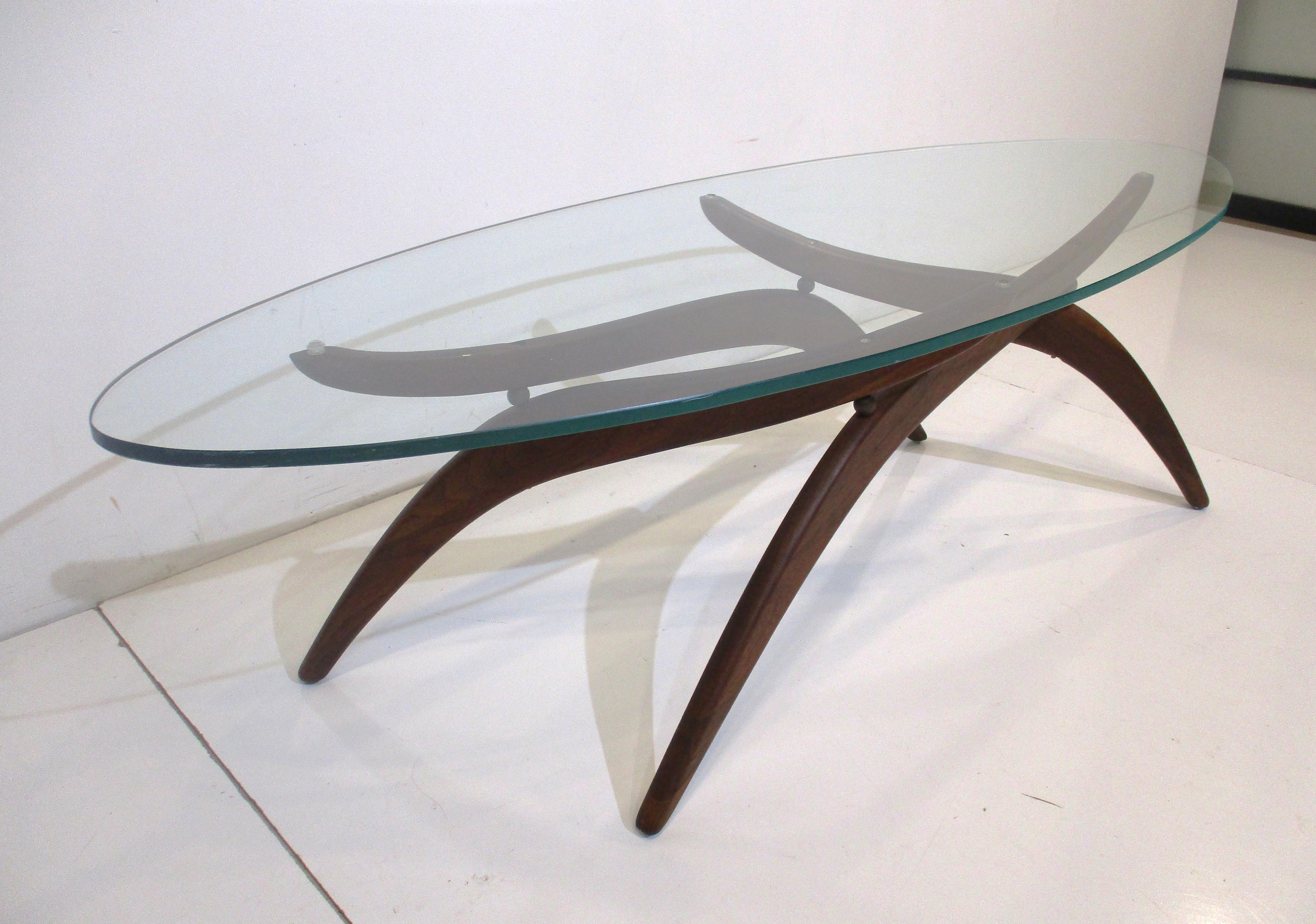 A sculptural solid walnut based Mid Century two piece coffee table with oval glass top designed by Forest Wilson . The base does fold slightly so the table can have a wider or narrower look and is manufactured in the manner of Adrian Pearsall . The