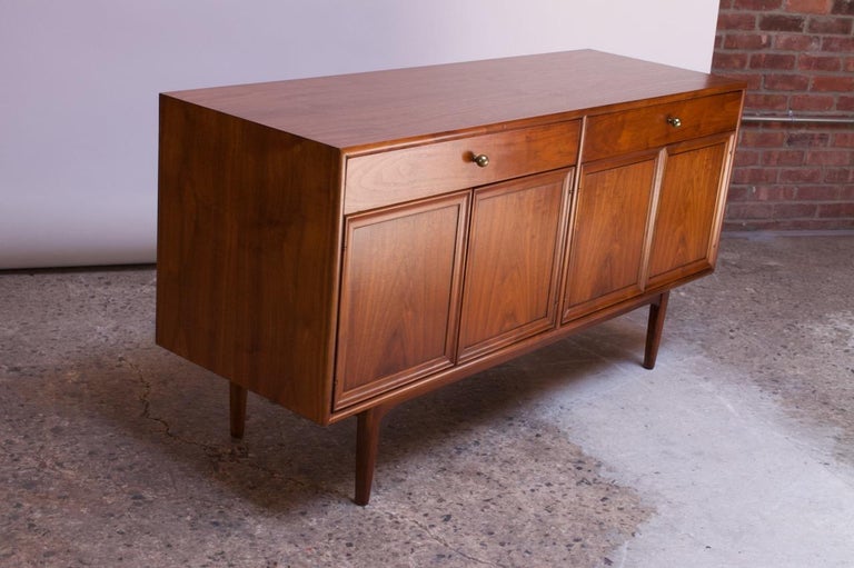 1950s walnut credenza / sideboard designed by Kipp Stewart for Drexel’s “Declaration” line. Composed of two sets of hinged doors which open to reveal a single, removable shelf per side with a light that automatically turns on when the doors are