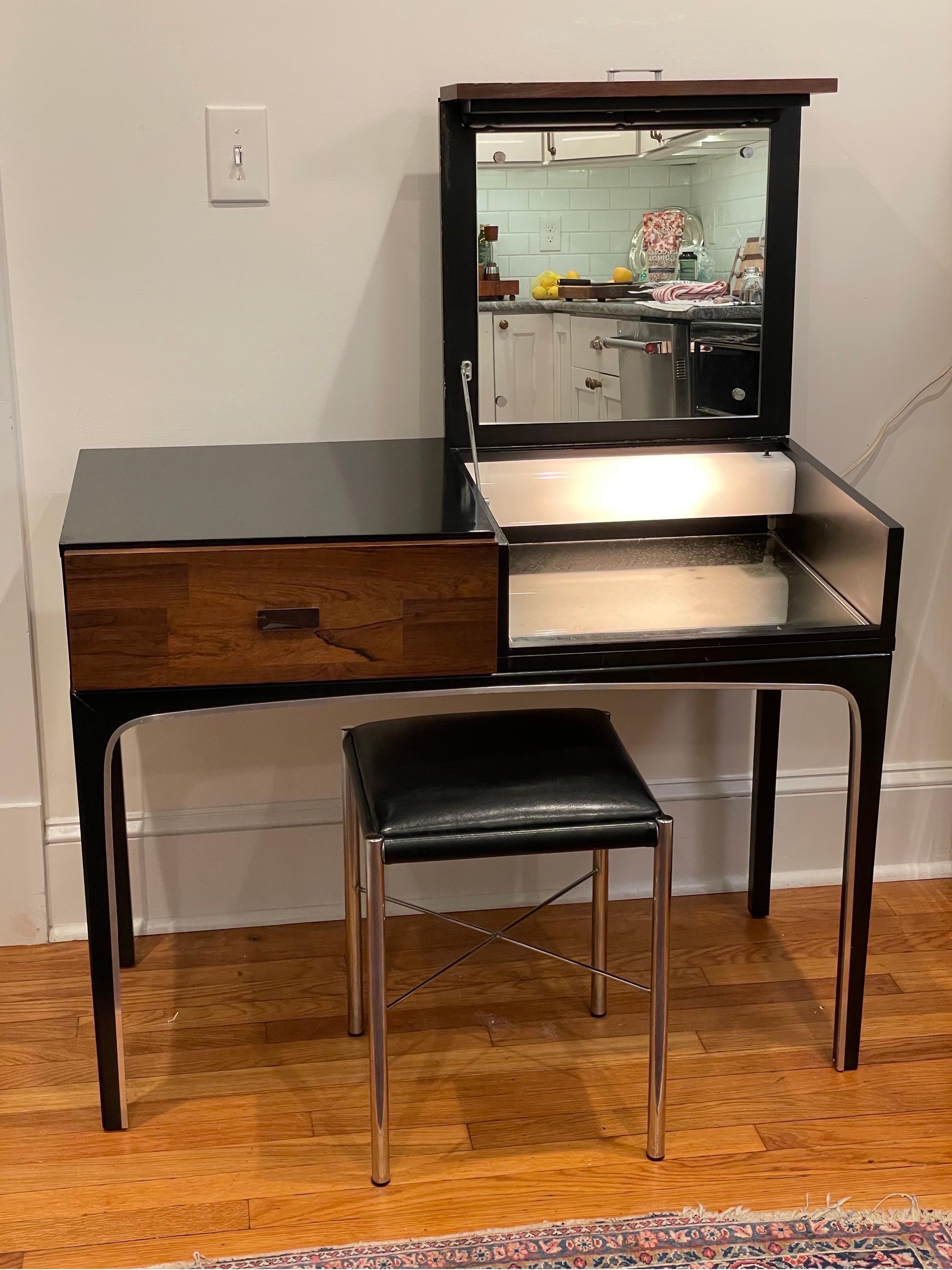 Unique mid century lift top lighted vanity in the manner of Milo Baughman. Beautiful sleek detail with classic contrasting wood, lacquer and chrome. Right side lifts to expose lighted mirrored compartment. Left side offers a drawer for ample