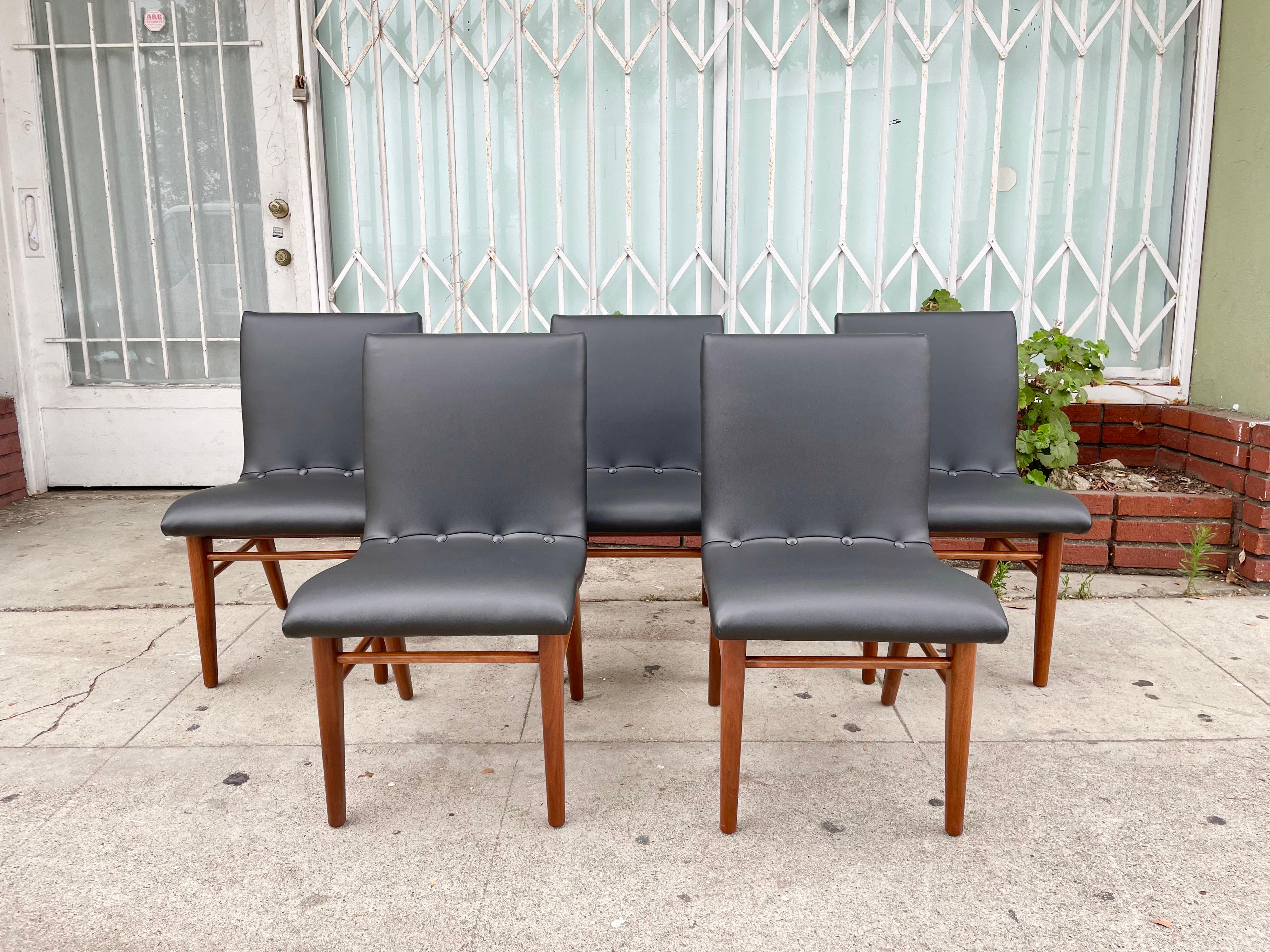 Midcentury walnut and leatherette dining chairs were manufactured in the United States, circa the 1950s. These vintage dining chairs feature a solid walnut base that has been refinished and reupholstered in black leatherette, bringing it back to its